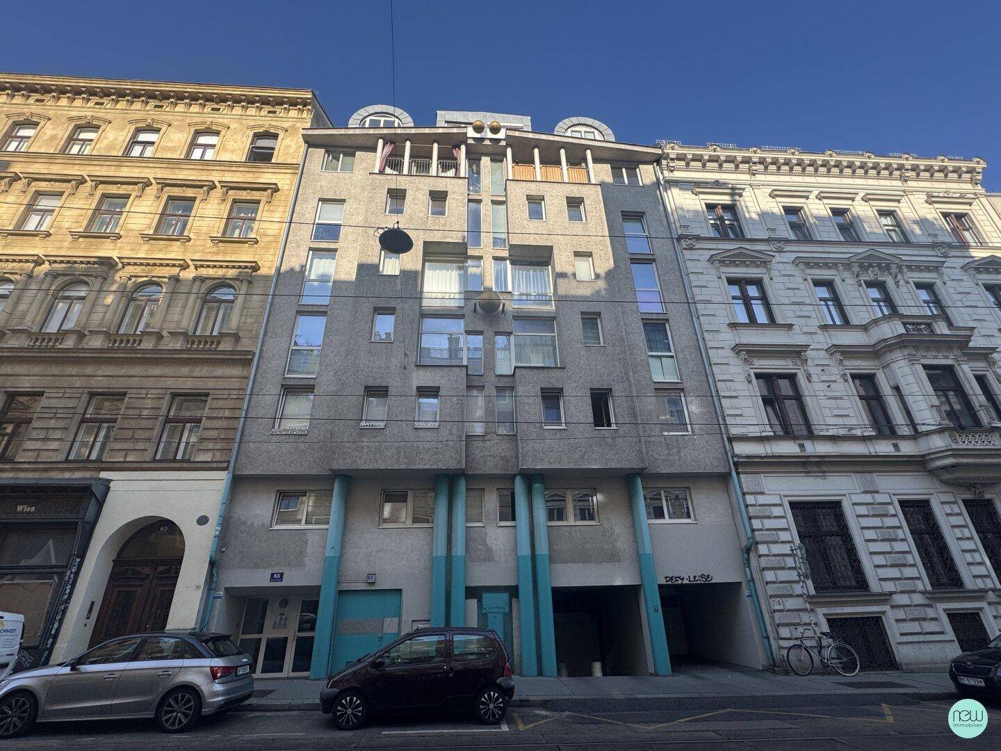 Moderne Gebäudefassade mit Balkonen und integrierter Tiefgarage, umgeben von historischen Altbauten in der Stadt.