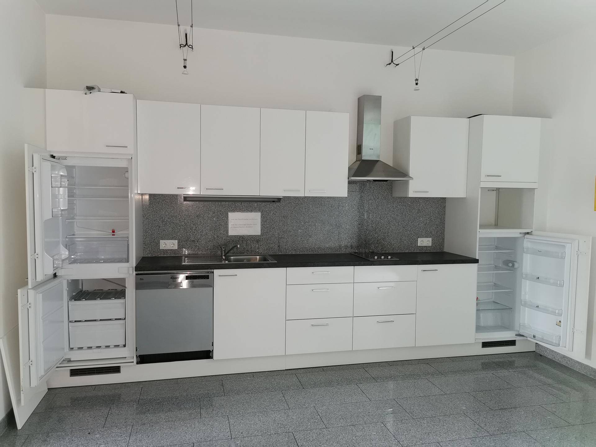 Moderne Einbauküche mit weißen Hochglanzfronten, Edelstahlgeräten und Fliesenboden.