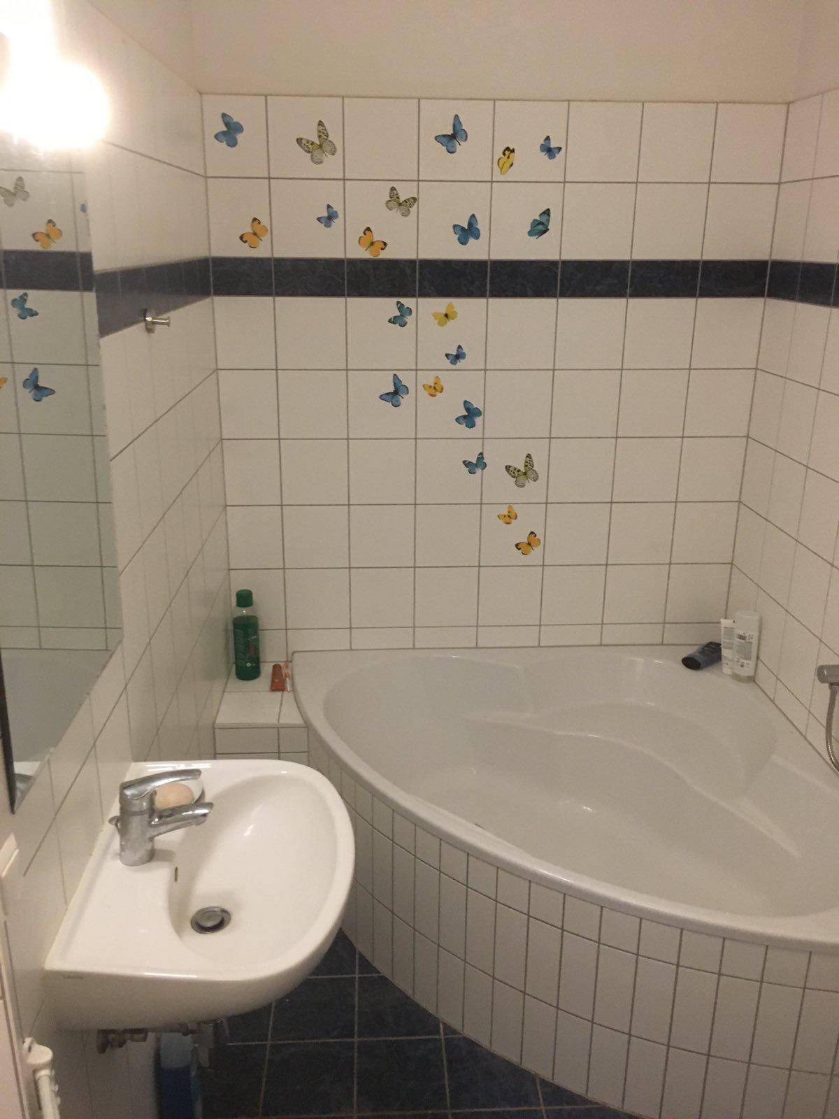 Badezimmer mit Eckbadewanne, Waschbecken und Spiegel, verziert mit bunten Schmetterlingsstickern.