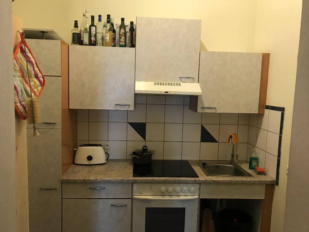 Kleine Küche mit Einbauschränken, Kochfeld und Spüle, ausgestattet für den täglichen Gebrauch.