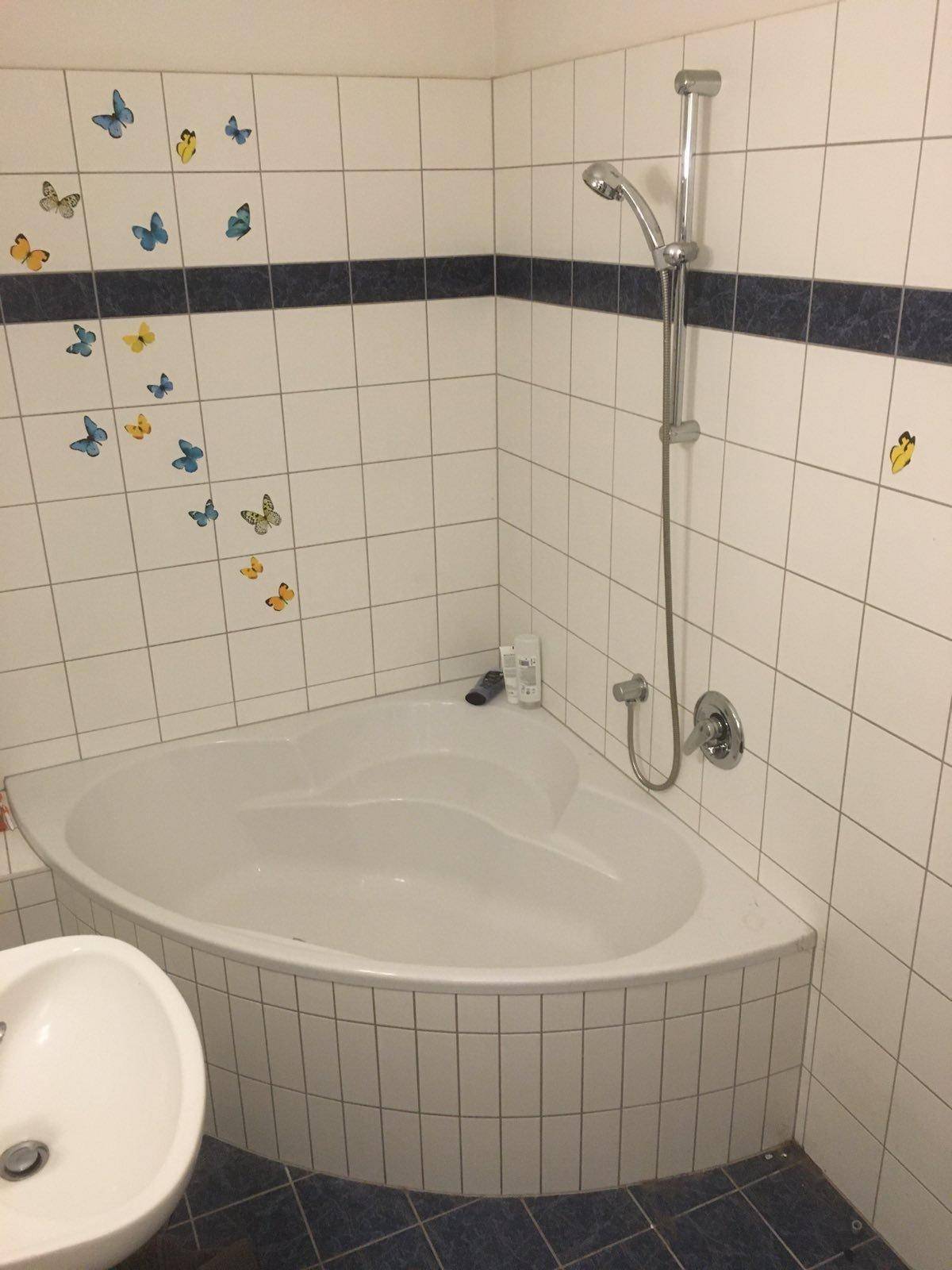 Eckbadewanne mit Duscharmatur in einem gefliesten Badezimmer, dekoriert mit Schmetterlingsmotiven.
