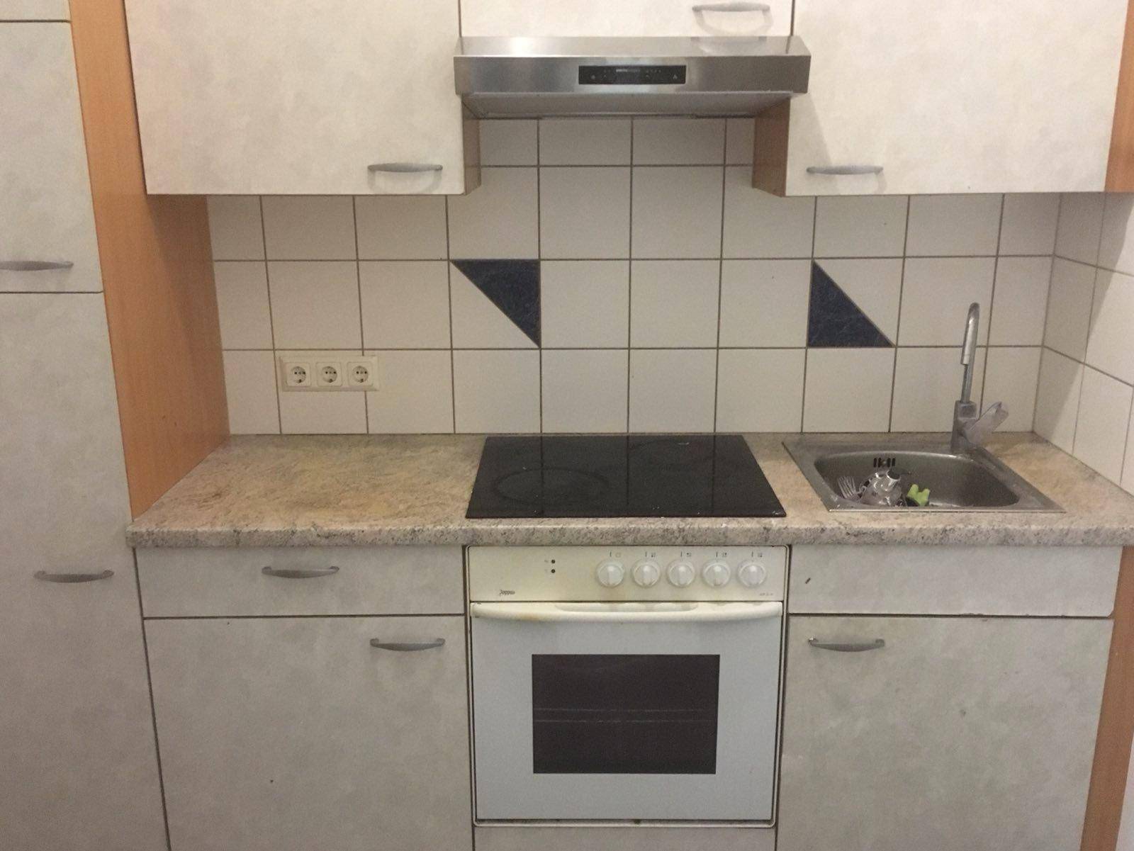 Küchenzeile mit Kochfeld, Backofen und Dunstabzugshaube, umgeben von hellen Schränken.