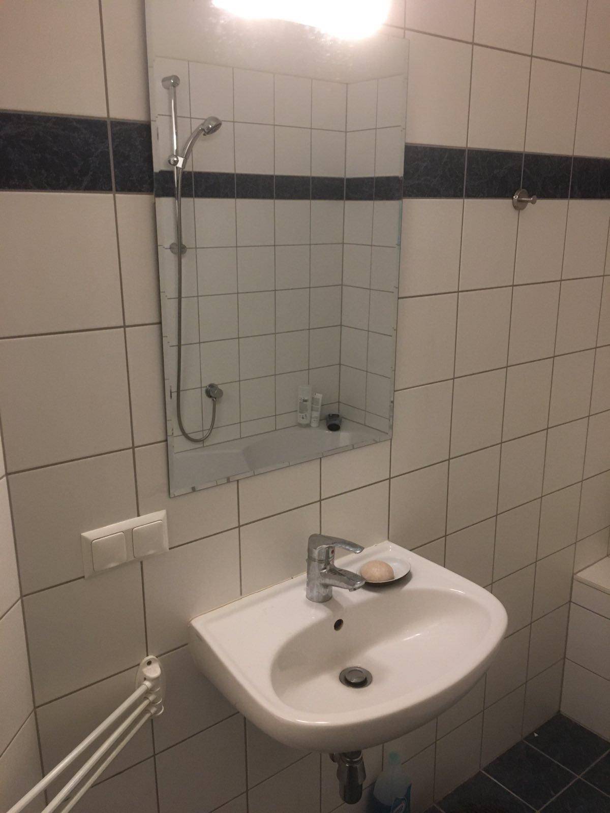 Badezimmer mit Waschbecken, Spiegel und weißen Fliesen, ergänzt durch eine dunkle Akzentlinie.