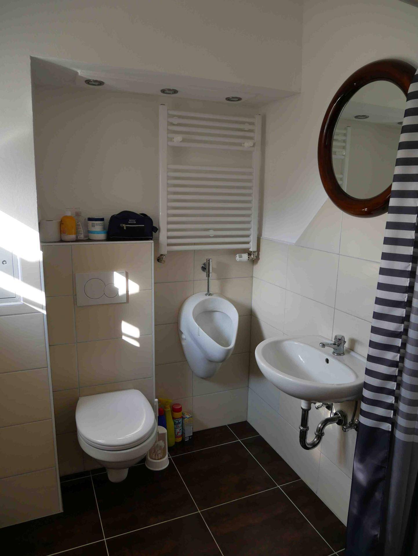 Kleines Badezimmer mit Urinal, Toilette, Waschbecken und beheiztem Handtuchhalter.
