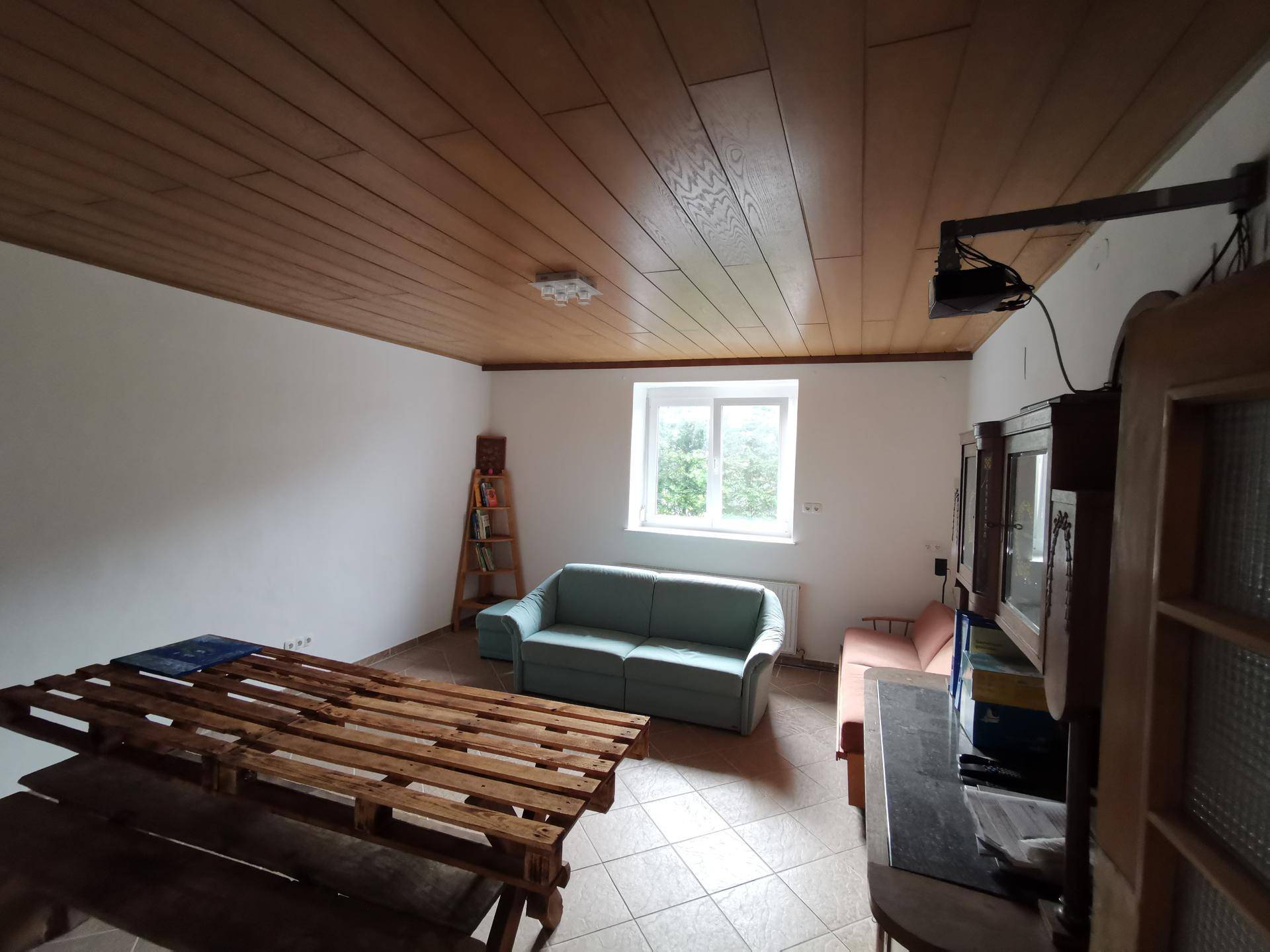 Geräumiges Wohnzimmer mit Holzdecke, Fliesenboden und einem Sofa, hell und einladend.