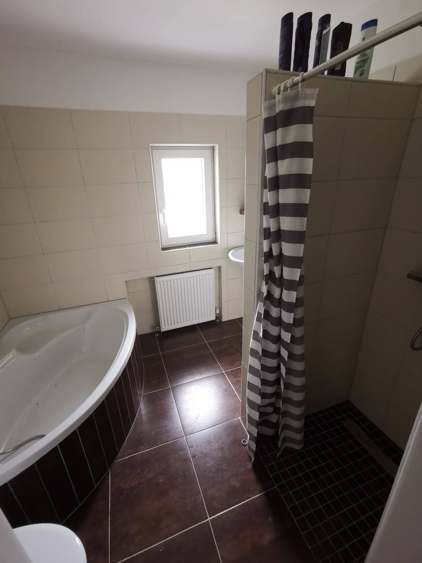 Badezimmer mit Eckbadewanne, Duschbereich und beigefarbenen Fliesen in gutem Zustand.