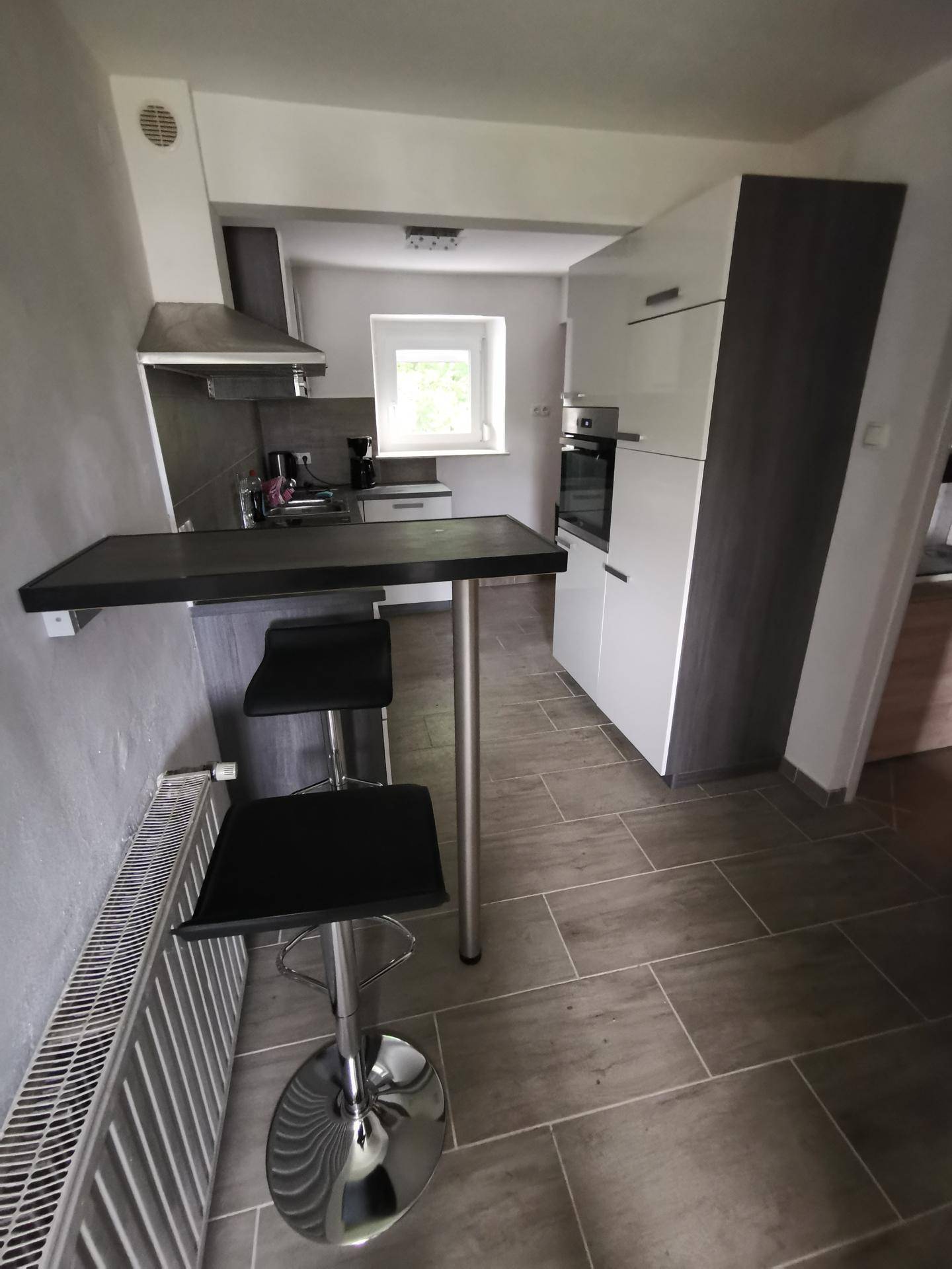 Moderne Küchenzeile mit Frühstücksbar, weißen und grauen Schränken und Fliesenboden.