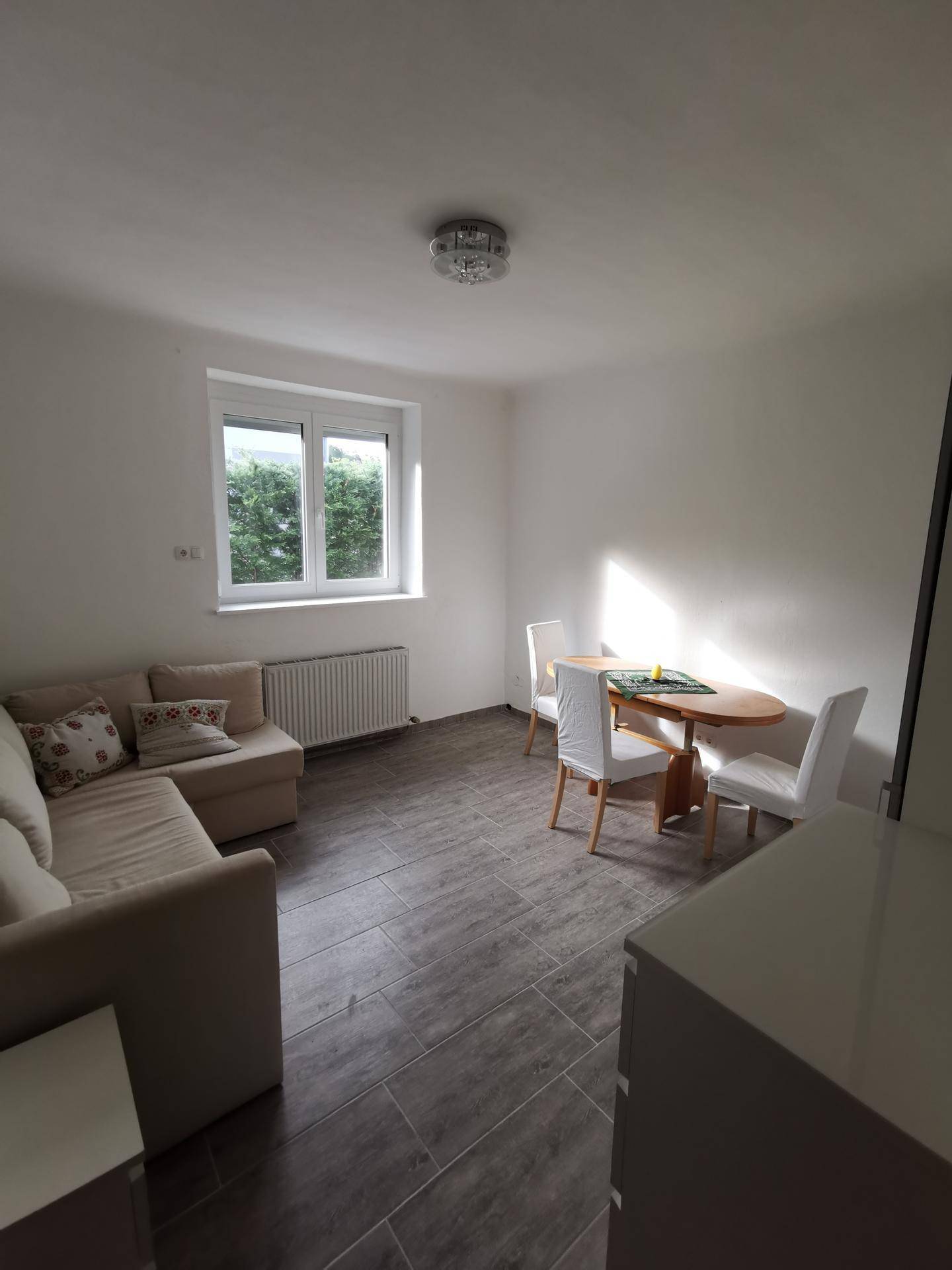Heller Wohn- und Essbereich mit Sofa, Esstisch und Fliesenboden in Holzoptik.