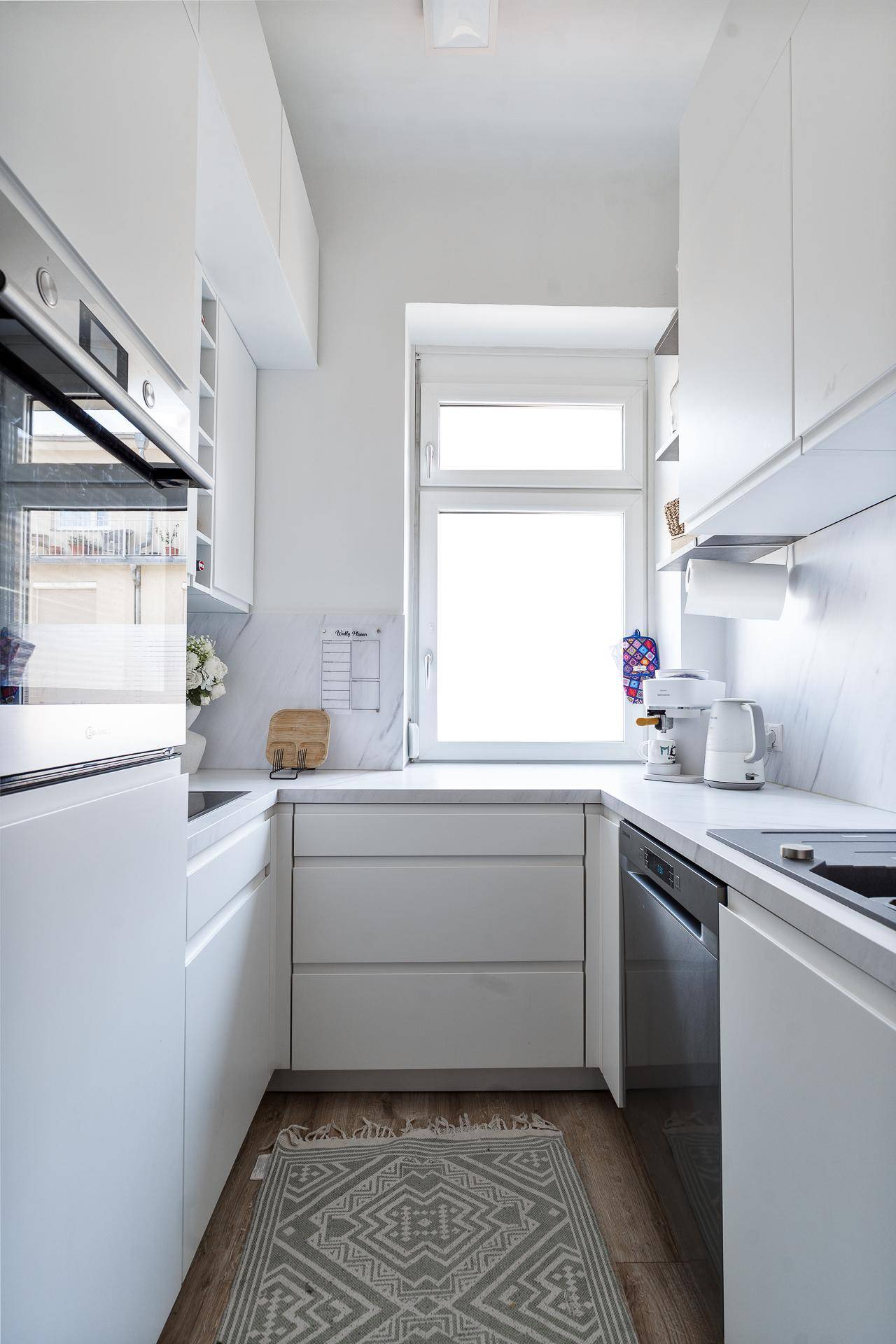 Funktionale weiße Küche mit modernen Geräten, Fenster und Holzboden.