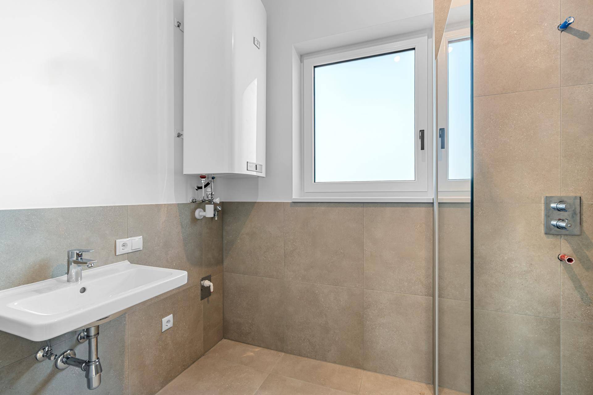 Modernes Badezimmer mit Waschtisch, Fenster und Wandfliesen, inklusive Warmwasserbereiter.