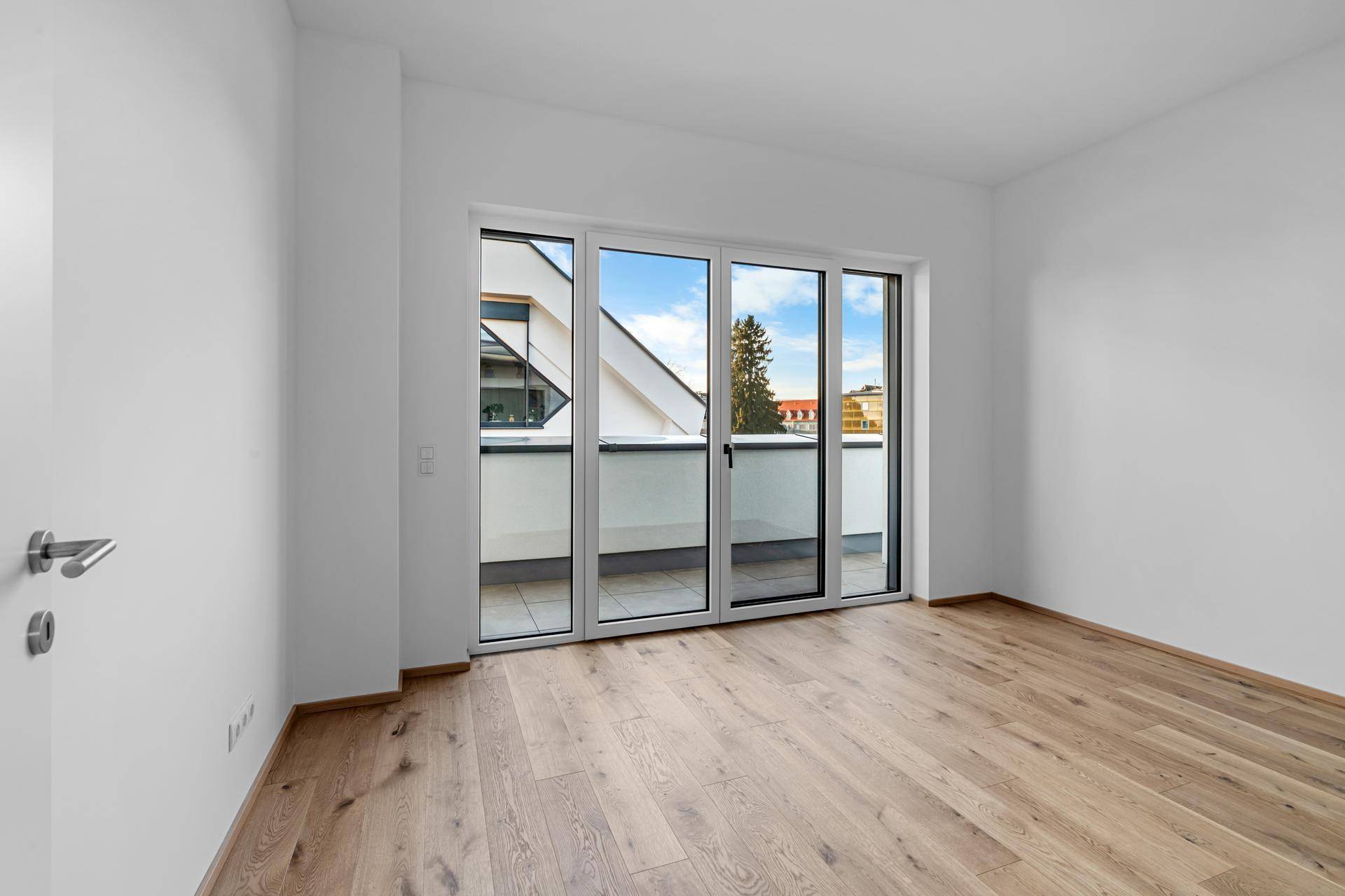 Geräumiges Schlafzimmer mit hellem Holzparkett und Balkonzugang durch große Fenstertüren.