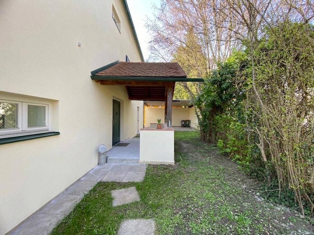 Seitlicher Eingangsbereich des Hauses mit überdachtem Vordach und einem kleinen Gartenweg.