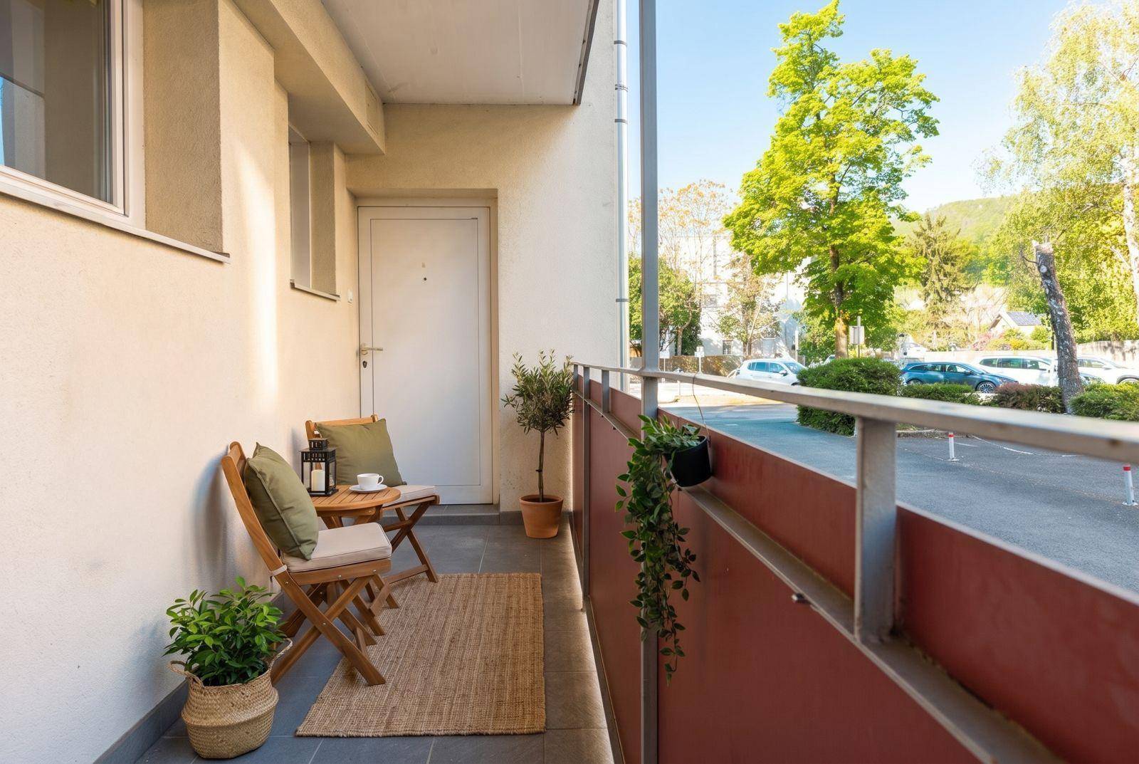 Gemütlicher Balkon mit Sitzgelegenheiten, Pflanzen und Blick auf die Straße und Bäume.