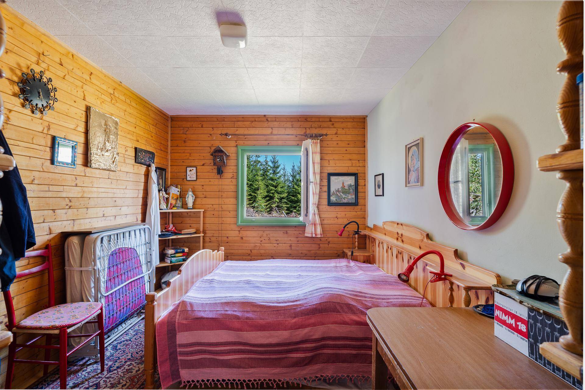 Schlafzimmer mit Holzvertäfelung, Doppelbett und einem Fenster mit Blick auf die umliegenden Bäume.