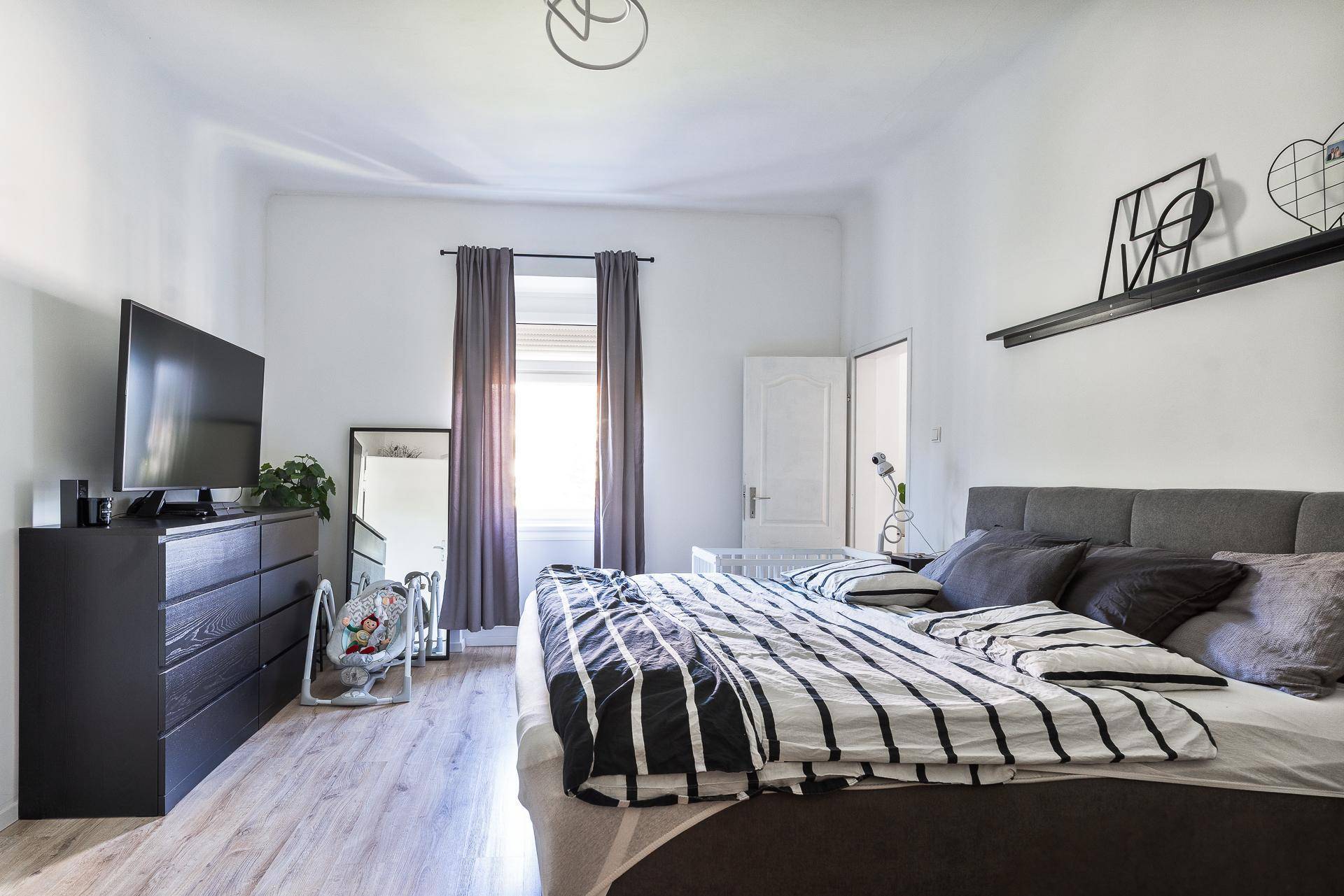 Helles Schlafzimmer mit Doppelbett, großem Spiegel und Fenster mit Vorhängen.