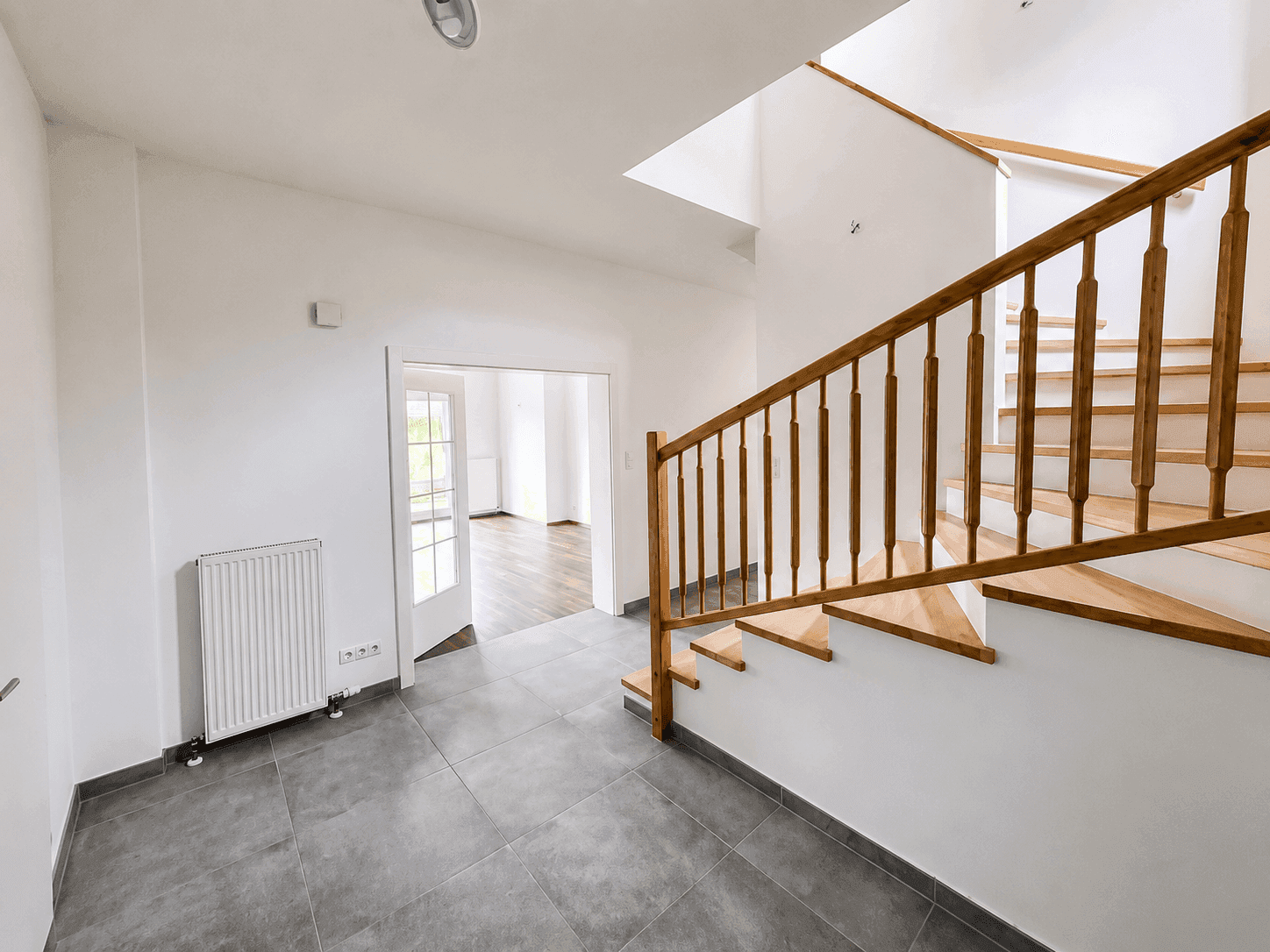 Heller Eingangsbereich mit moderner Holztreppe und großformatigen Fliesen.