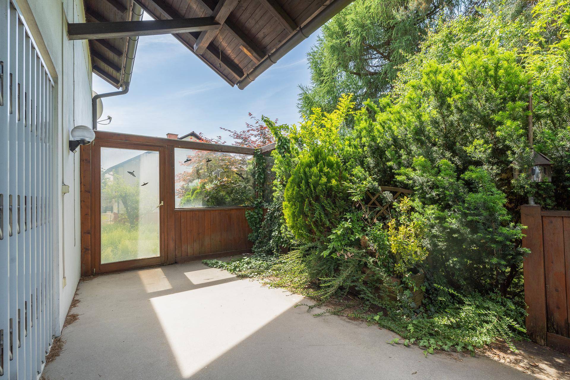 Überdachter Terrassenbereich mit Holzelementen und üppiger grüner Bepflanzung.