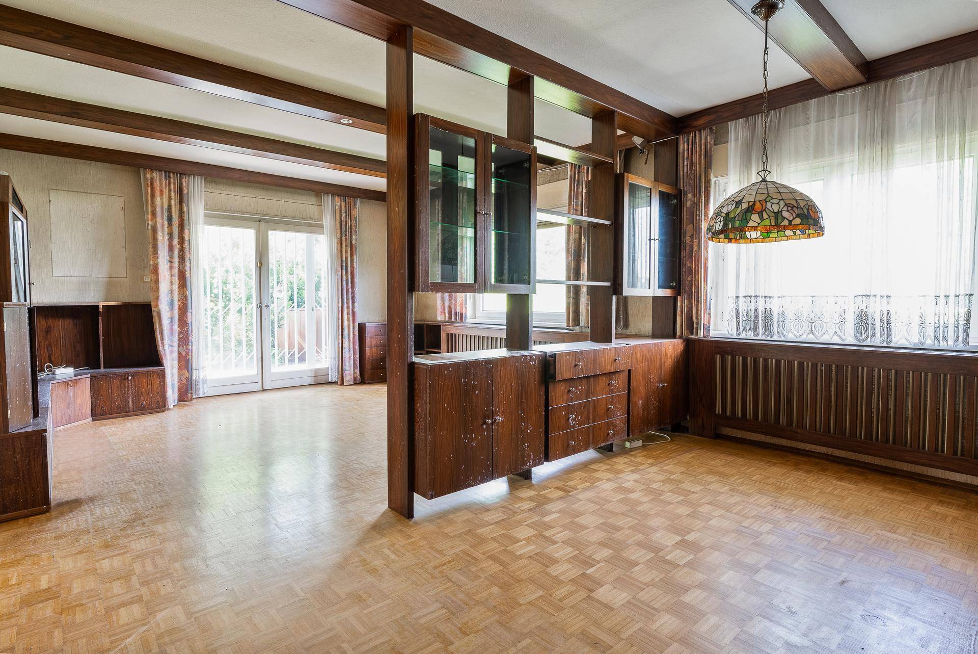 Großes Wohnzimmer mit Holzbalken, Parkettboden und dekorativer Raumteilung.