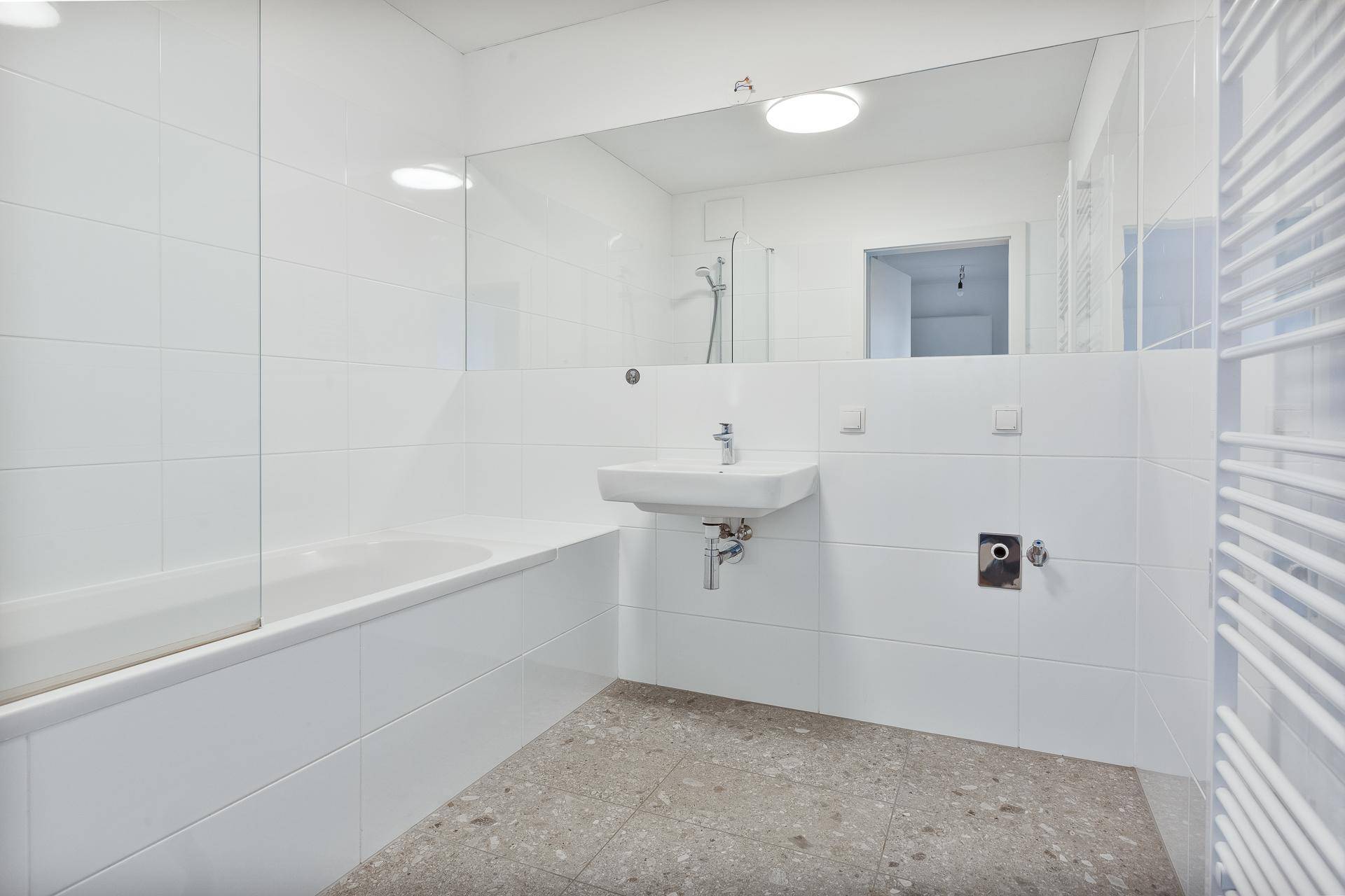 Modernes Badezimmer mit weißen Fliesen, Badewanne und großem Spiegel.