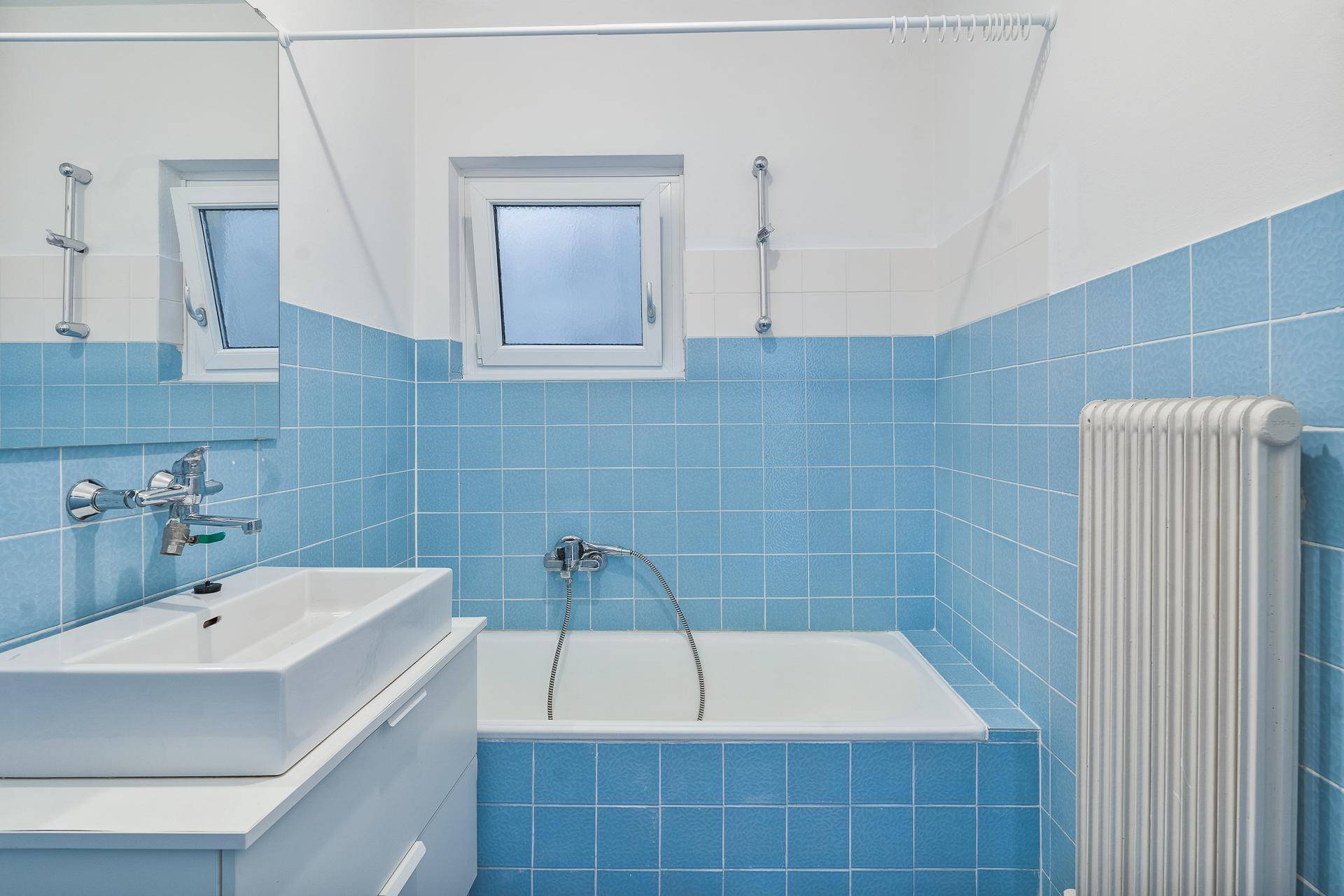 Badezimmer mit blauen Fliesen, Badewanne und Fenster für natürliche Belüftung.