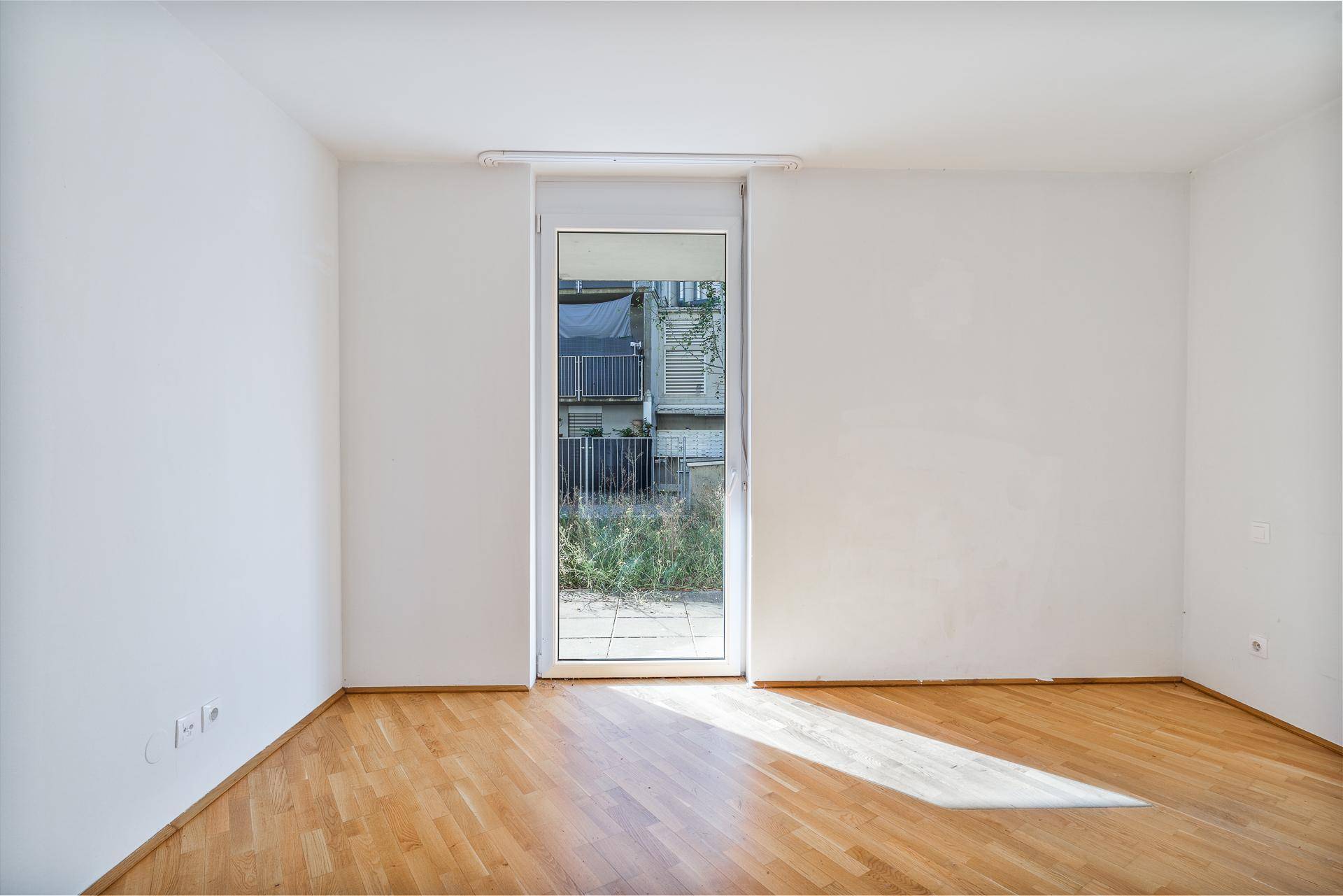 Geräumiger, heller Raum mit Parkettboden und Zugang zu einem Balkon oder einer Terrasse.