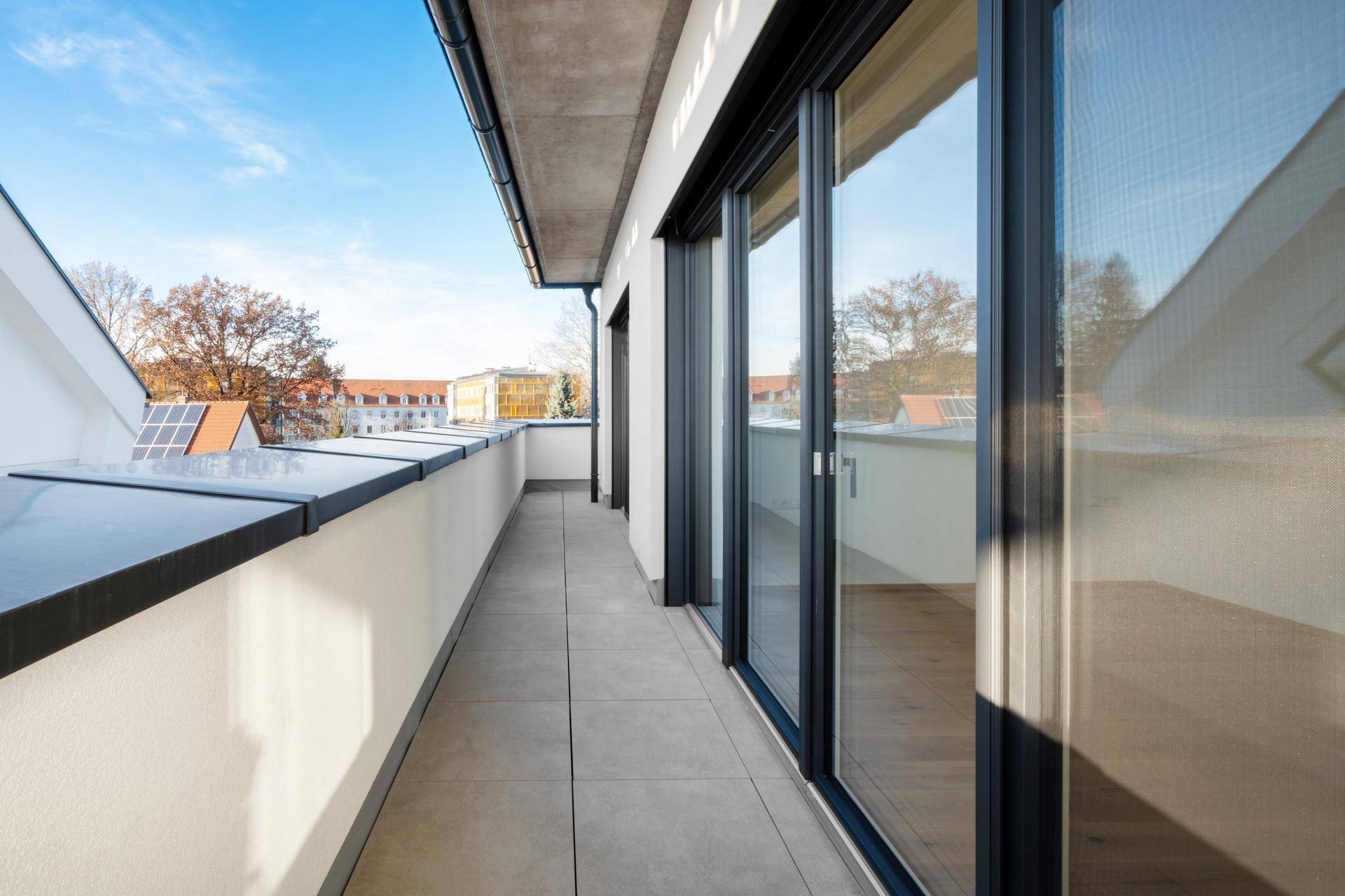 Schmaler Balkon mit Fliesenboden und Schiebetüren, der Zugang zu den Innenräumen bietet.