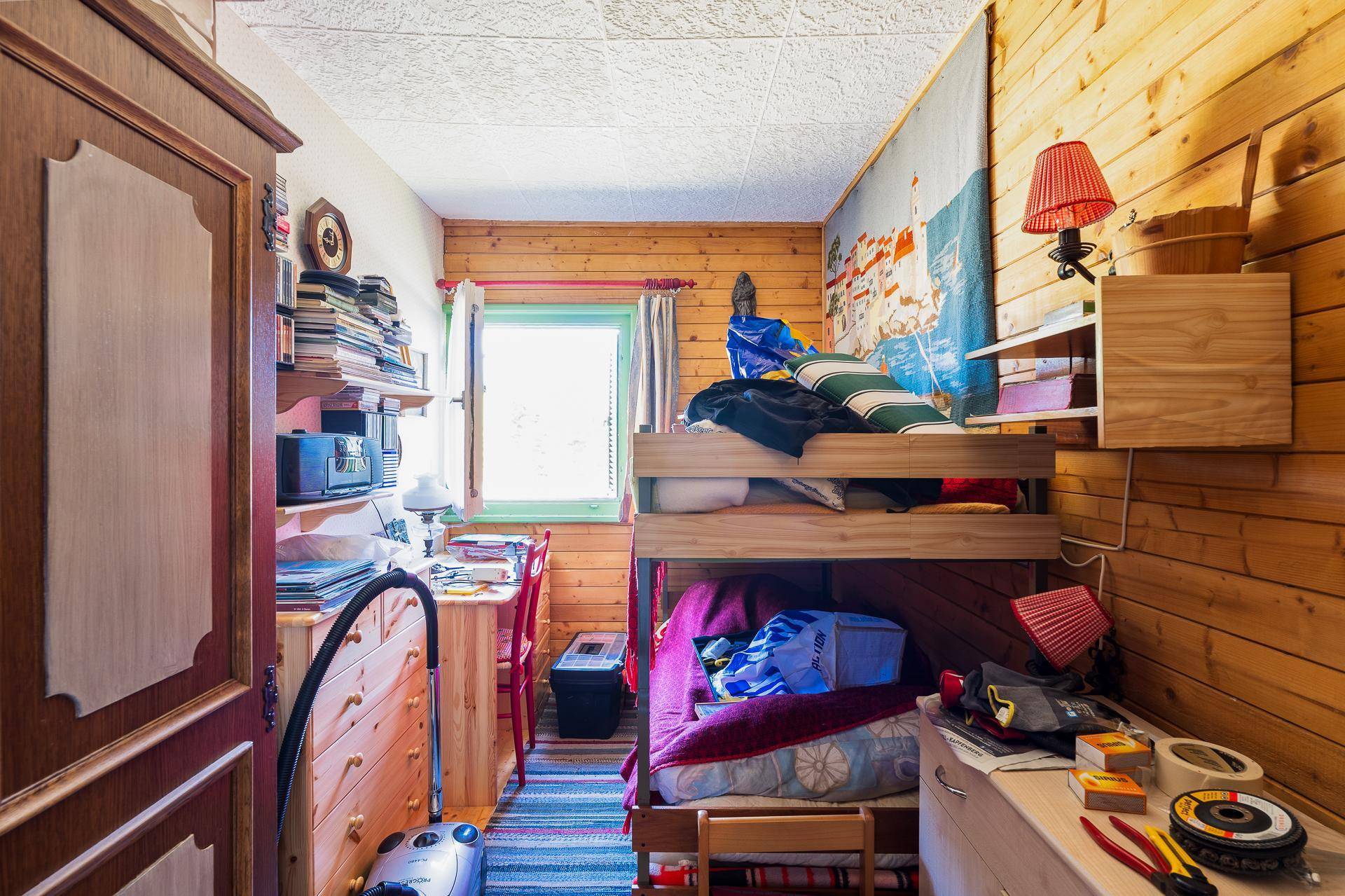 Kinderzimmer mit Etagenbett, Holzvertäfelung und einem Schreibtisch am Fenster.
