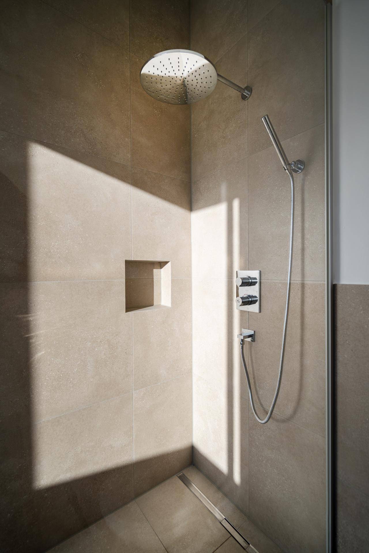 Moderne begehbare Dusche mit Regenduschkopf und integrierter Nische in den Wandfliesen.