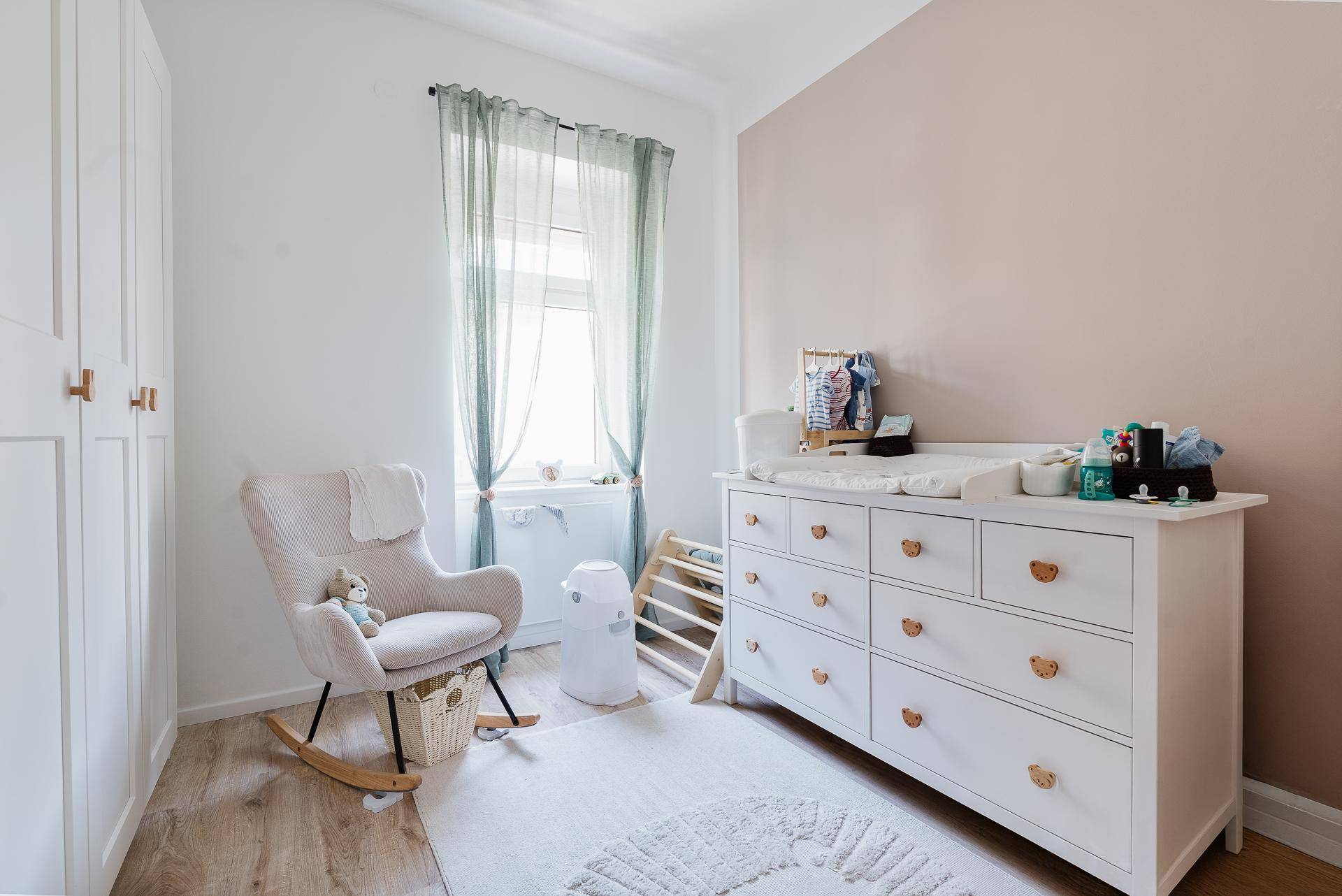 Helles Kinderzimmer mit Wickelkommode, Schaukelstuhl und Holzboden.