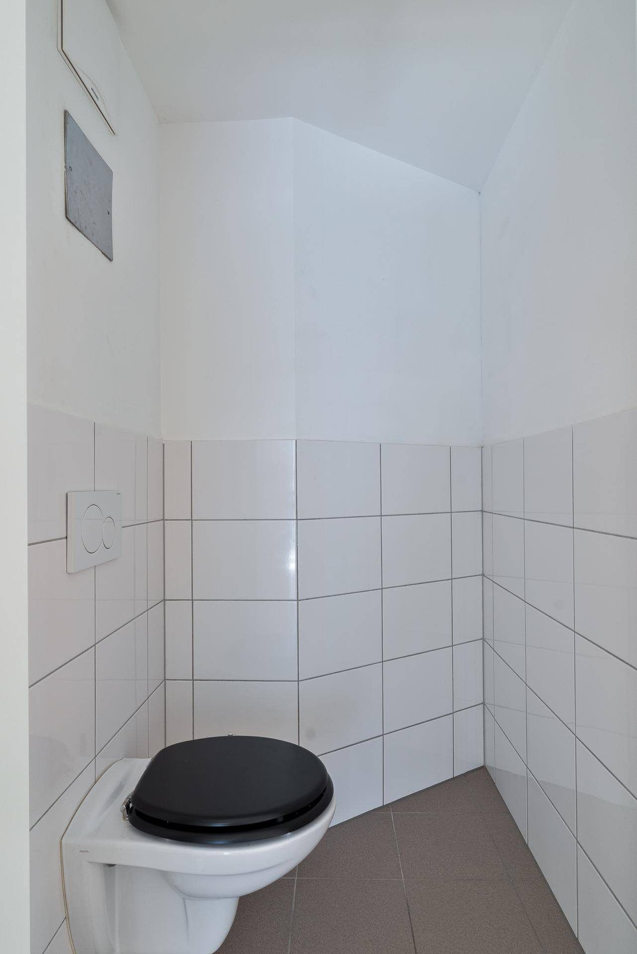 Kleines, weiß gefliestes Gäste-WC mit Wand-WC und dunklem Toilettensitz.