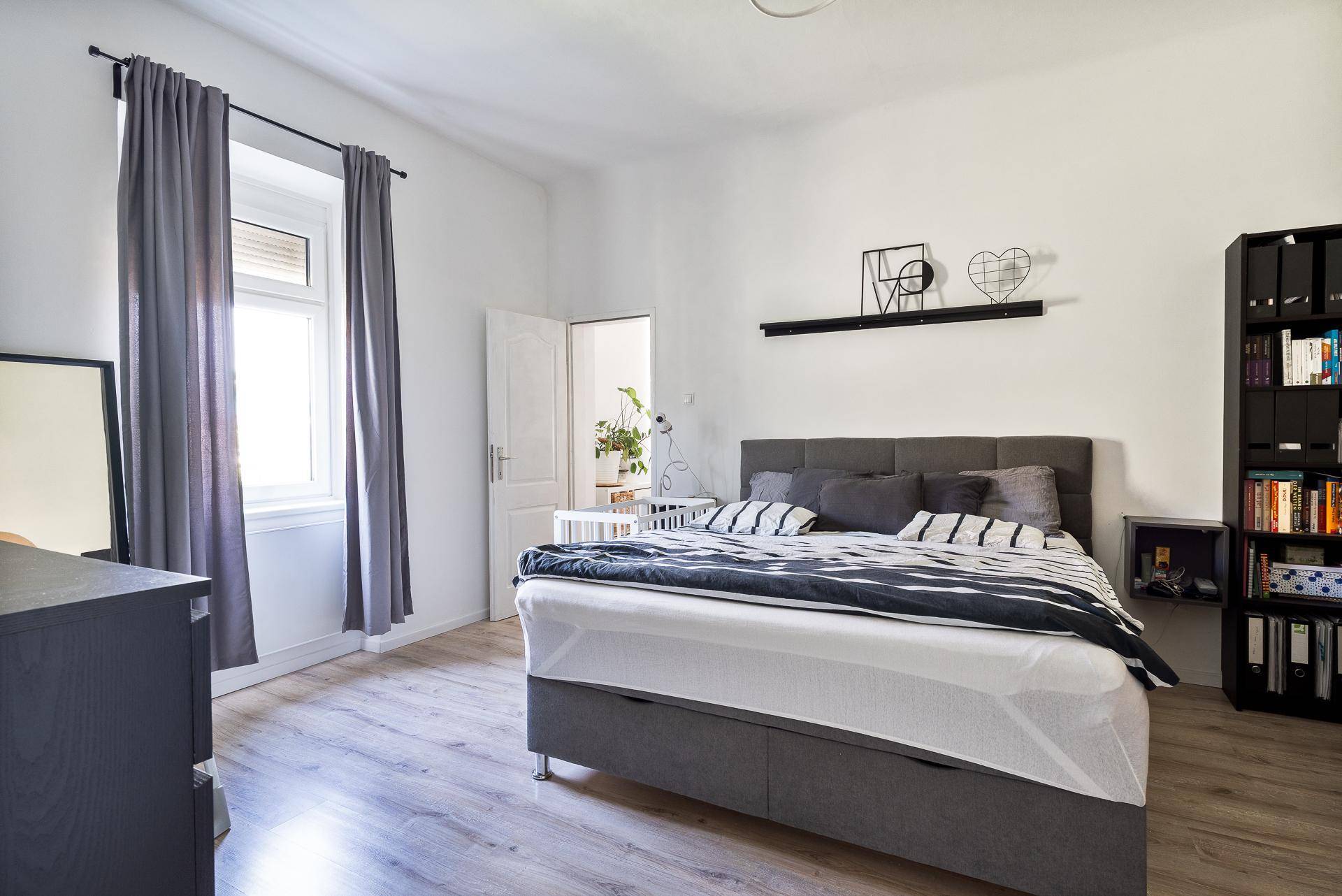 Schlafzimmer mit gemütlichem Doppelbett, Bücherregal und viel Tageslicht.