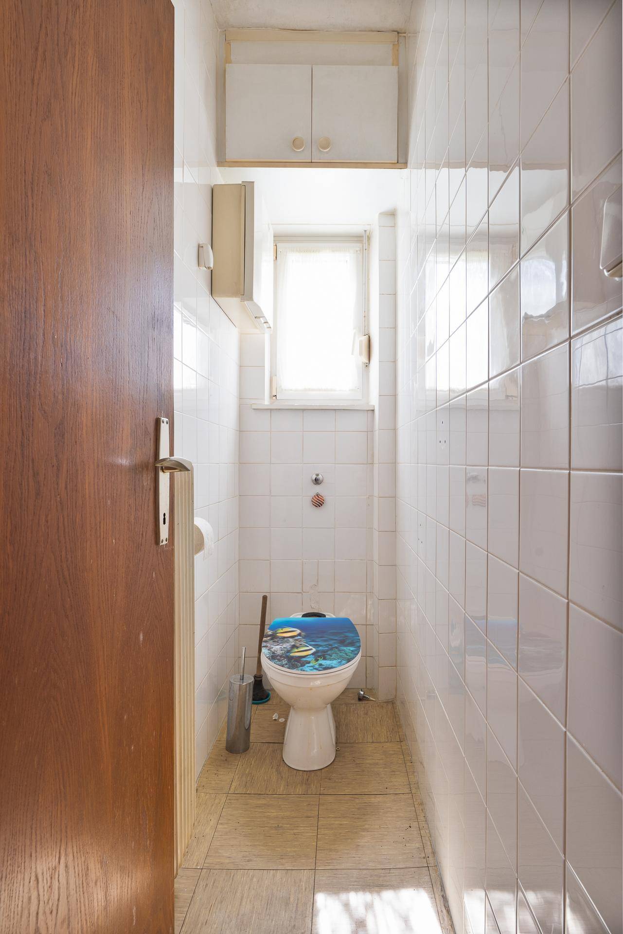 Separate Toilette mit Fenster und hellen Wandfliesen.