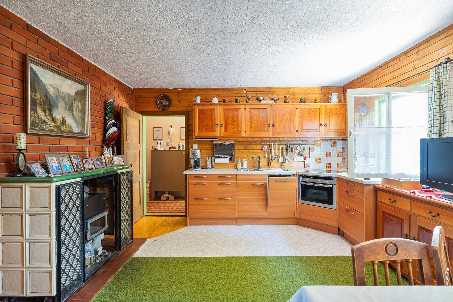 Traditionelle Küche mit Holzschränken, Backsteinwand und einem Kachelofen im Essbereich.