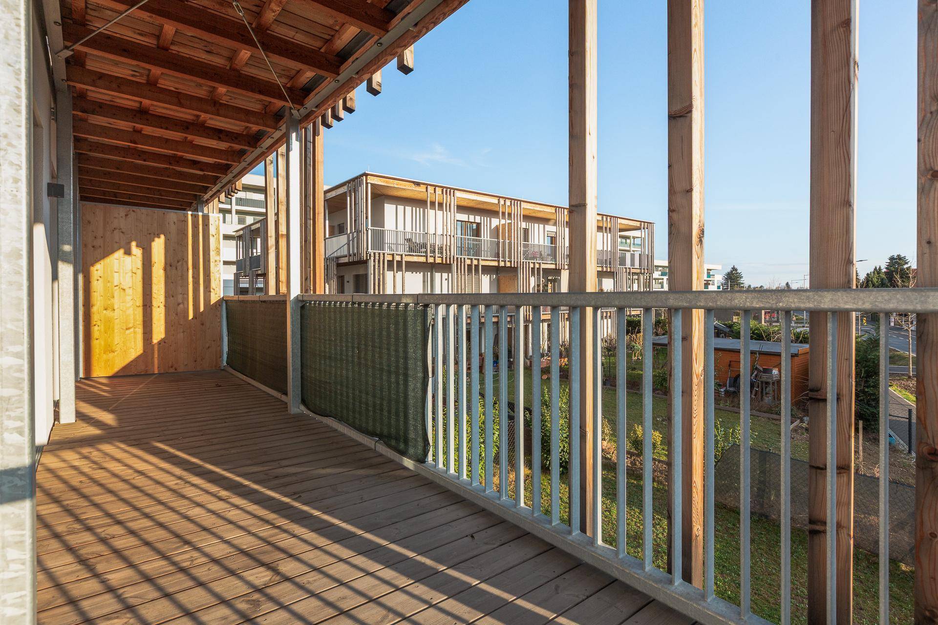 Geräumiger Balkon mit Holzboden und Blick auf die Umgebung und andere Gebäude.