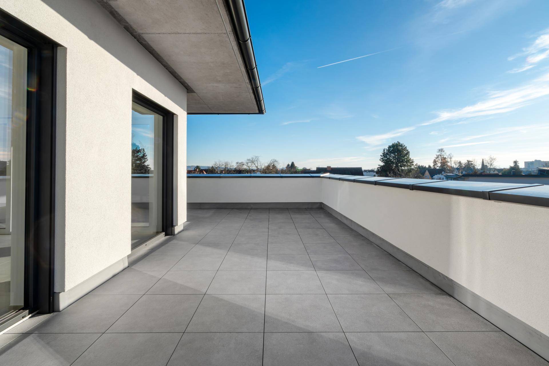 Geräumige Dachterrasse mit grauen Fliesen und Zugang zu den Innenräumen durch große Fenster.