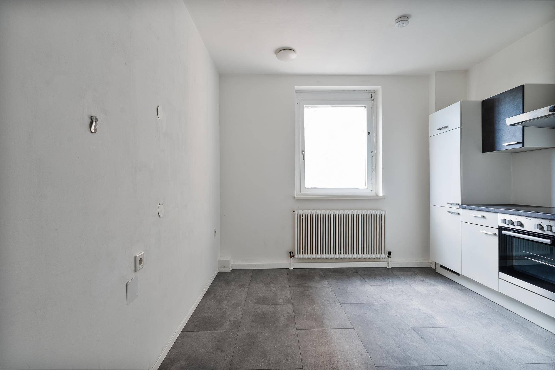 Helle Küche mit Fliesenboden und Fenster, bietet Platz für einen Essbereich.