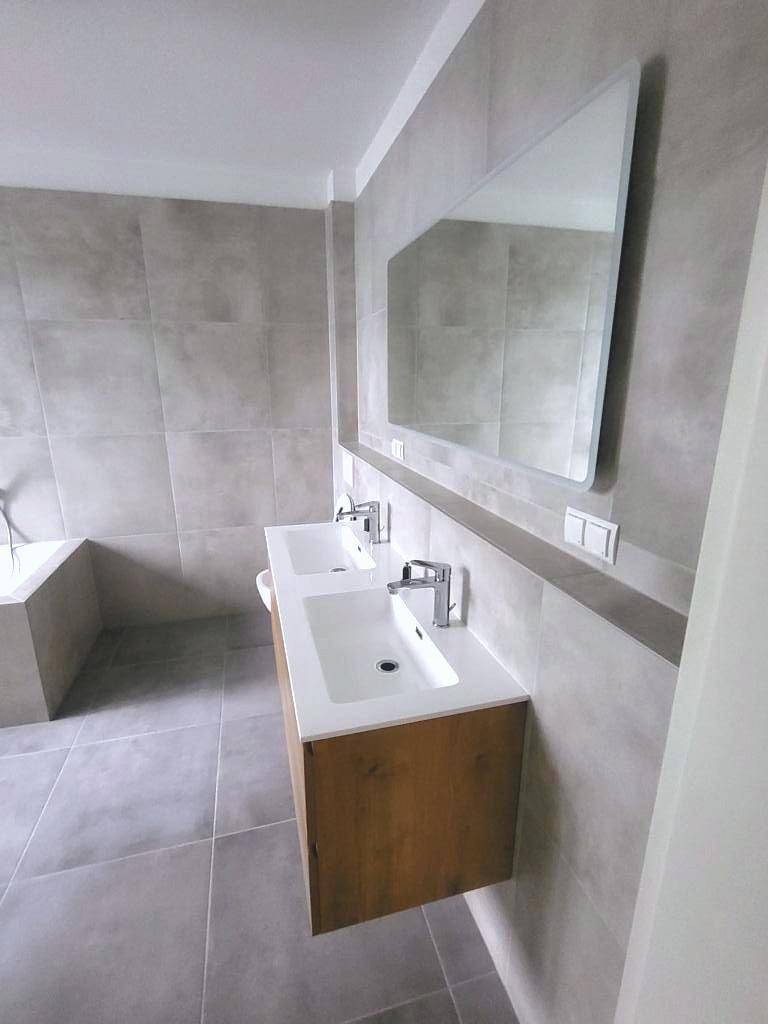 Elegantes Badezimmer mit Doppelwaschbecken und großem Spiegel, in neutralen Grautönen gehalten.