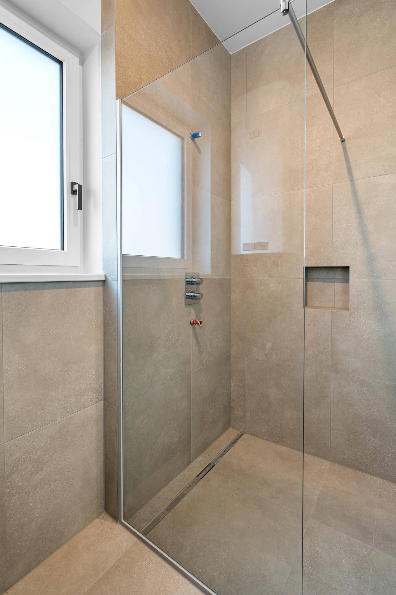 Begehbare Dusche mit Glasabtrennung und integrierter Nische in den Wandfliesen.