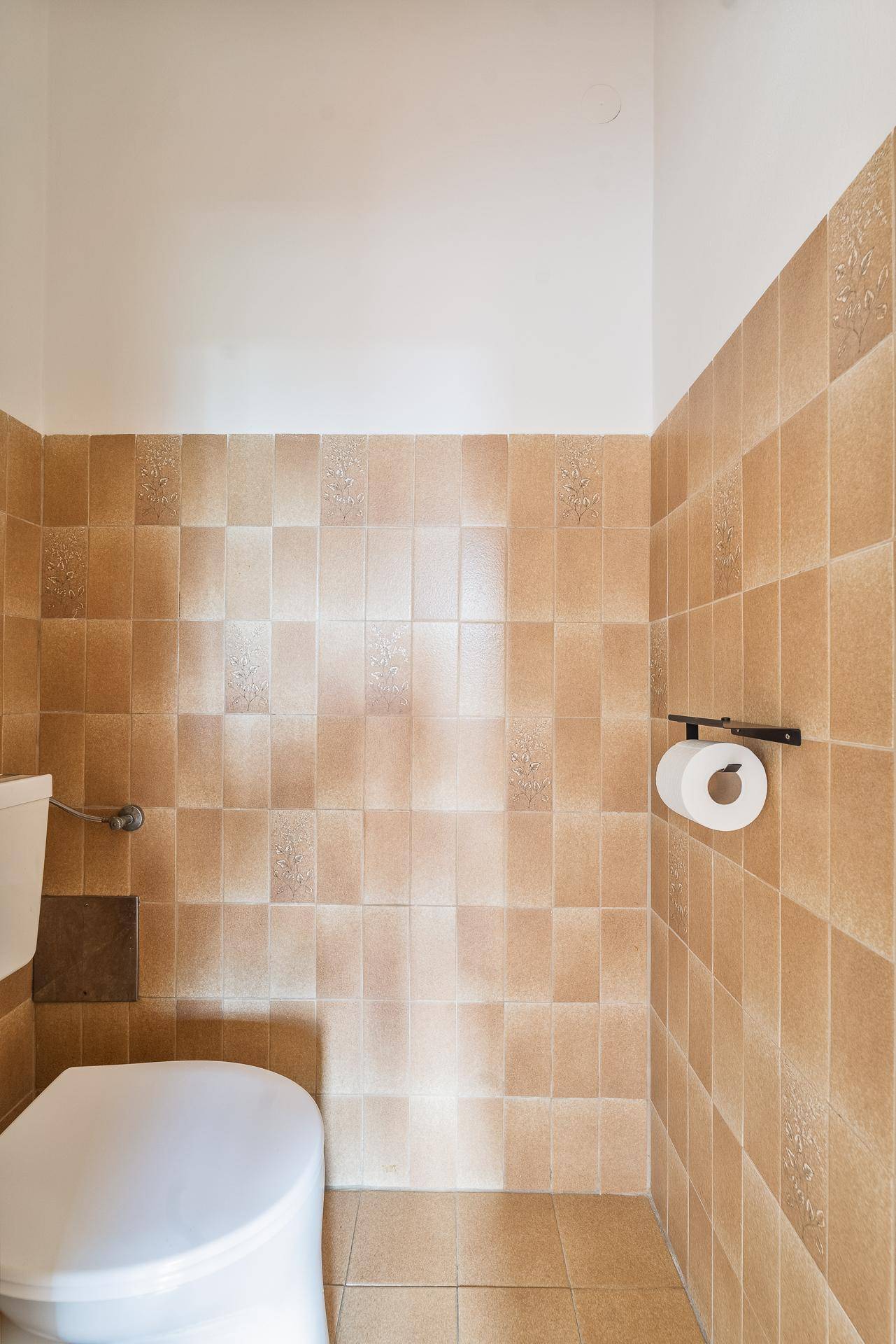 Separate Toilette mit beigefarbenen Fliesen und einfacher Ausstattung.