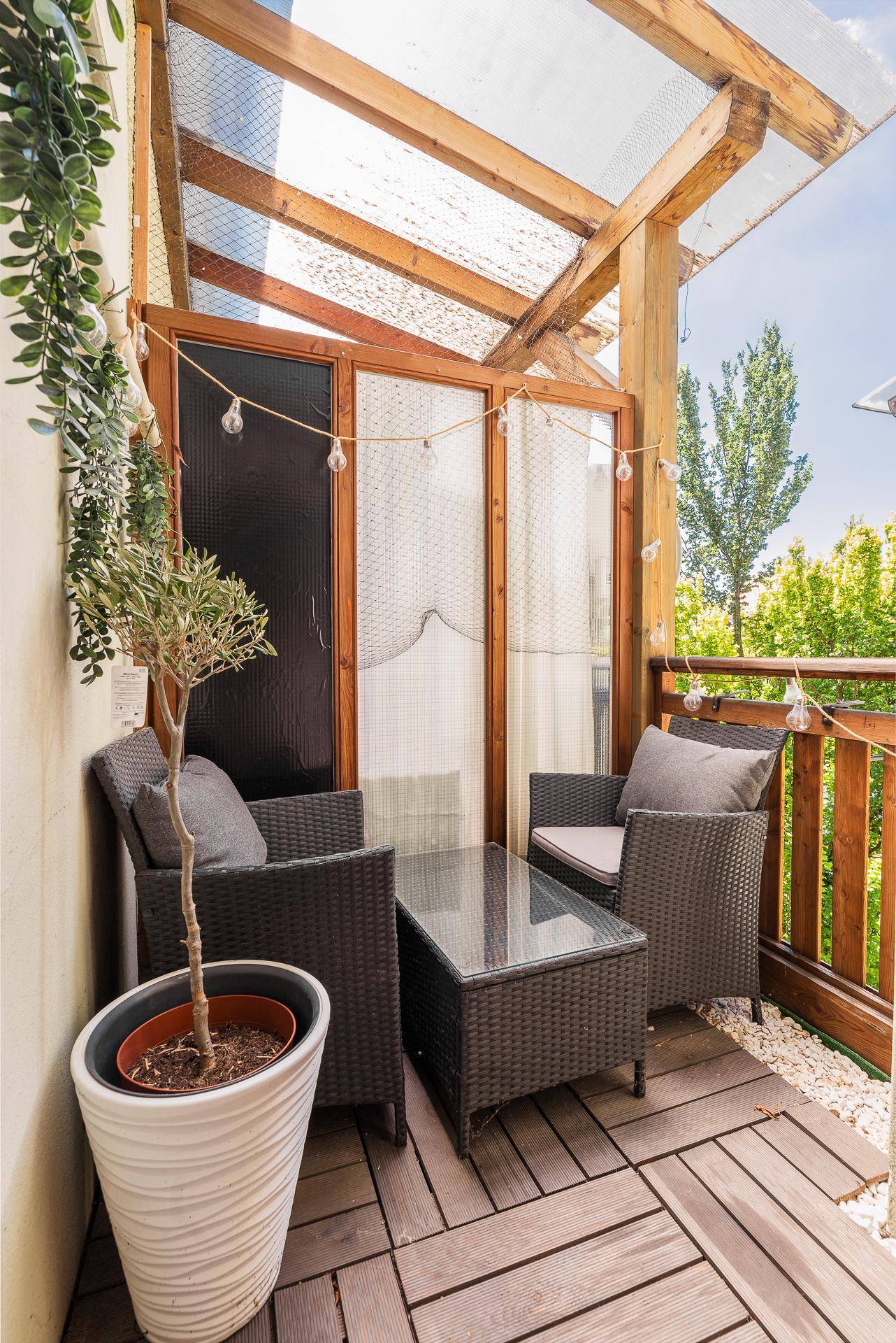 Sonniger Balkon mit Holzboden, gemütlichen Sitzgelegenheiten und Topfpflanzen.