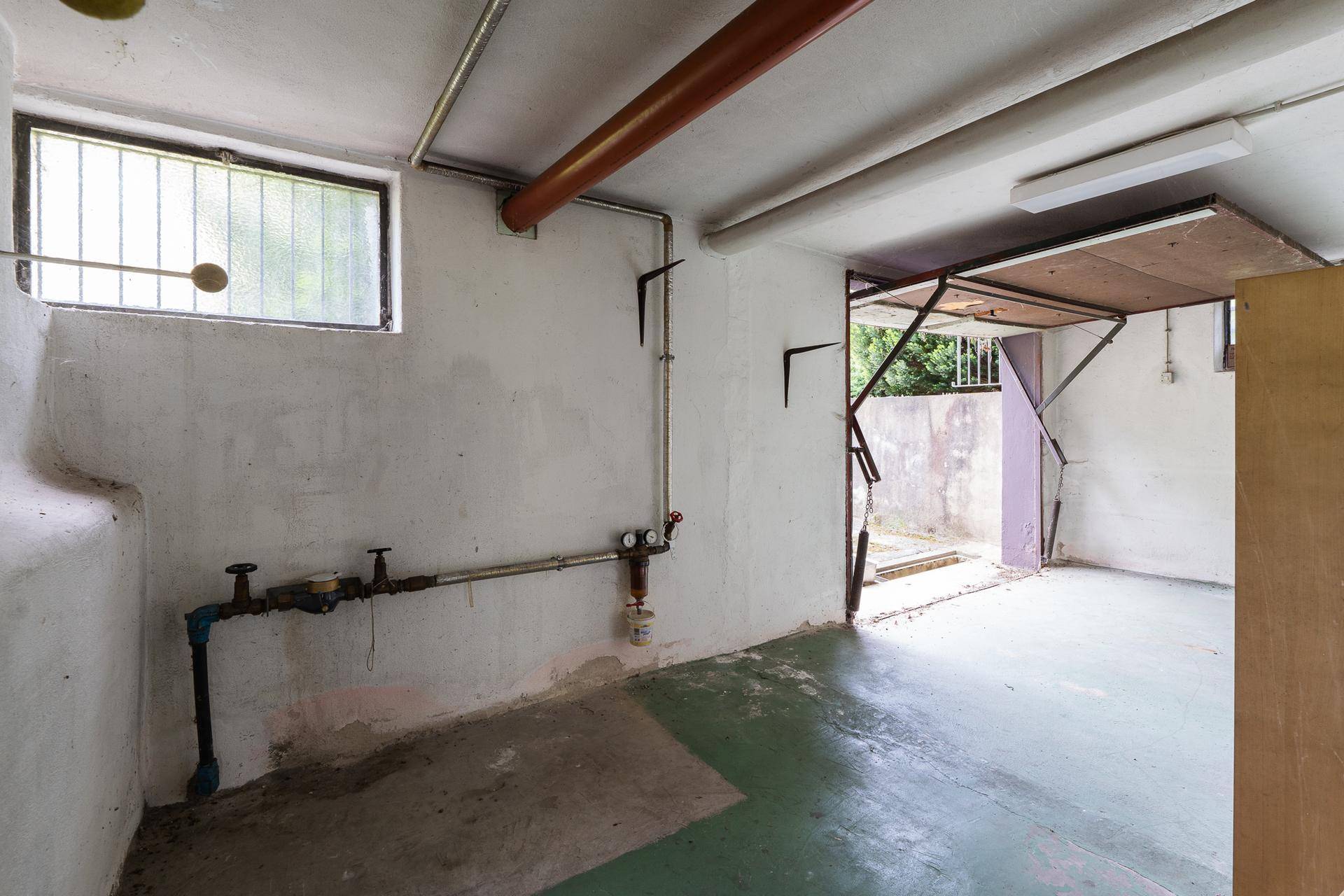 Kellerraum mit sichtbaren Rohren, Fenster und Zugang zur Außenseite.