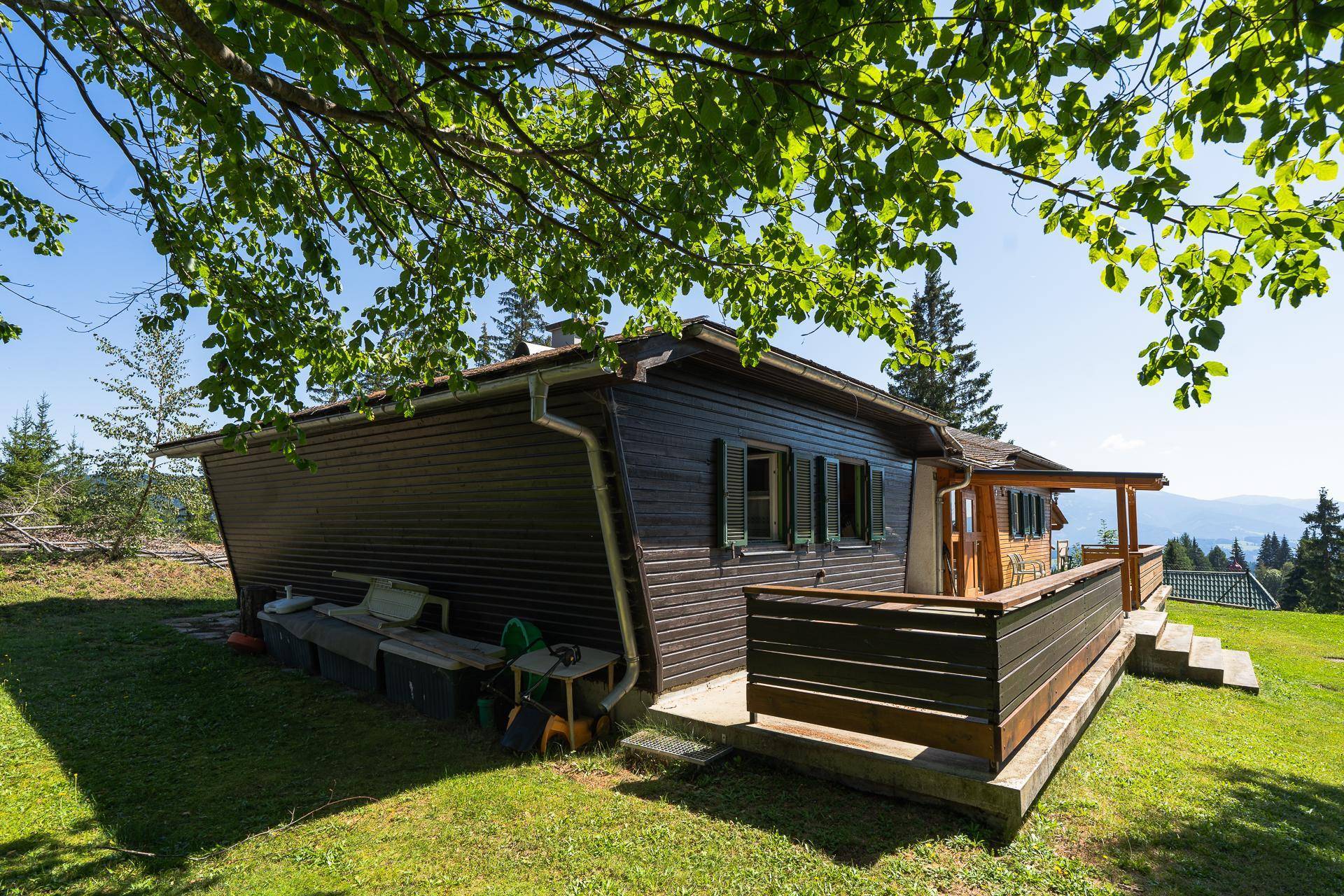 Das Haus von der Seite mit einem grünen Rasen und einer kleinen Terrasse unter Bäumen.