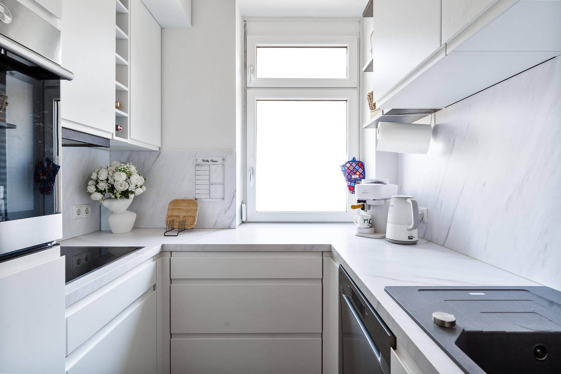 Moderne, helle Küche mit weißen Schränken, Einbaugeräten und Fenster.