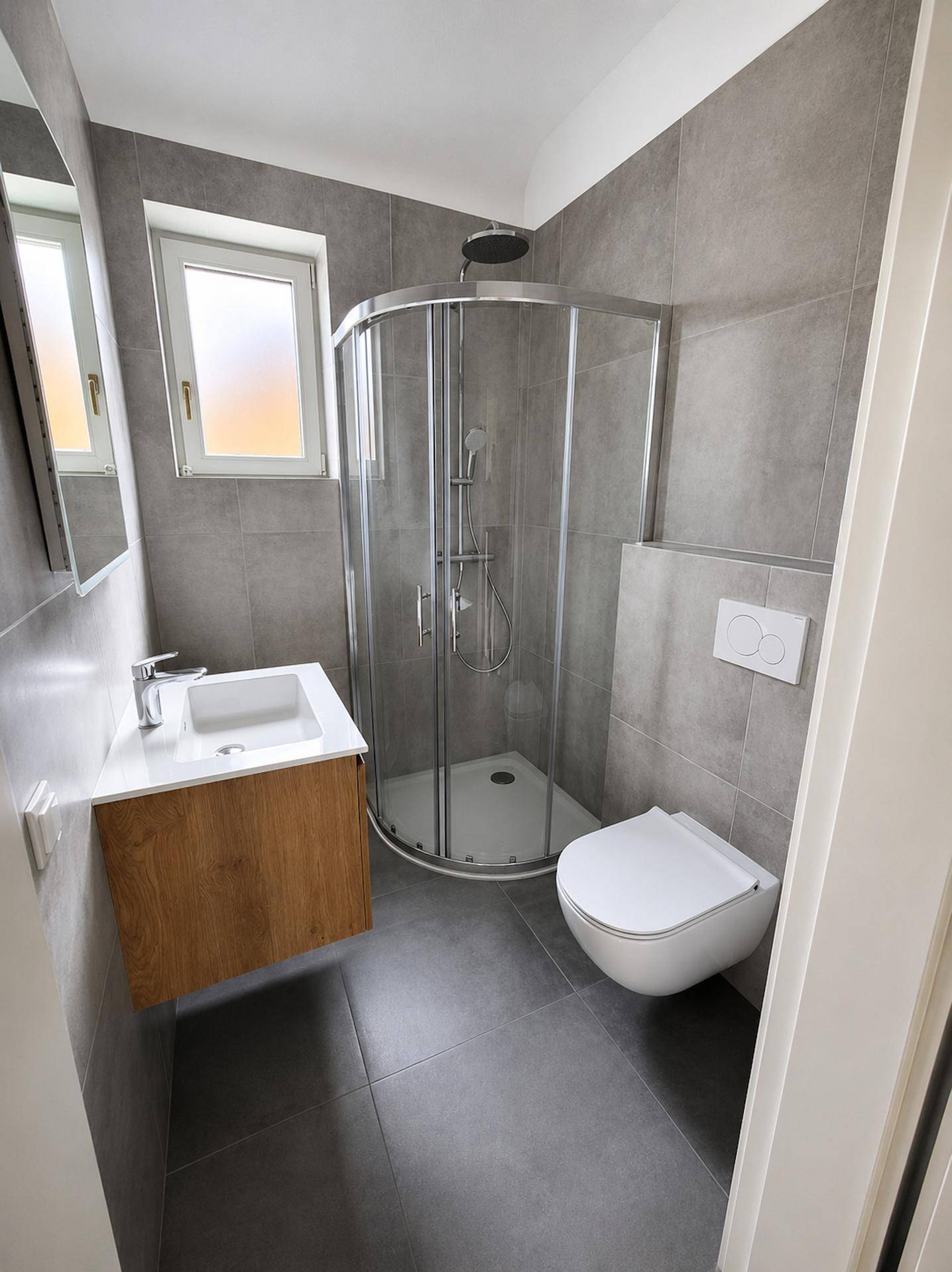 Kompaktes, modernes Badezimmer mit Eckdusche, Einzelwaschbecken und wandhängendem WC.
