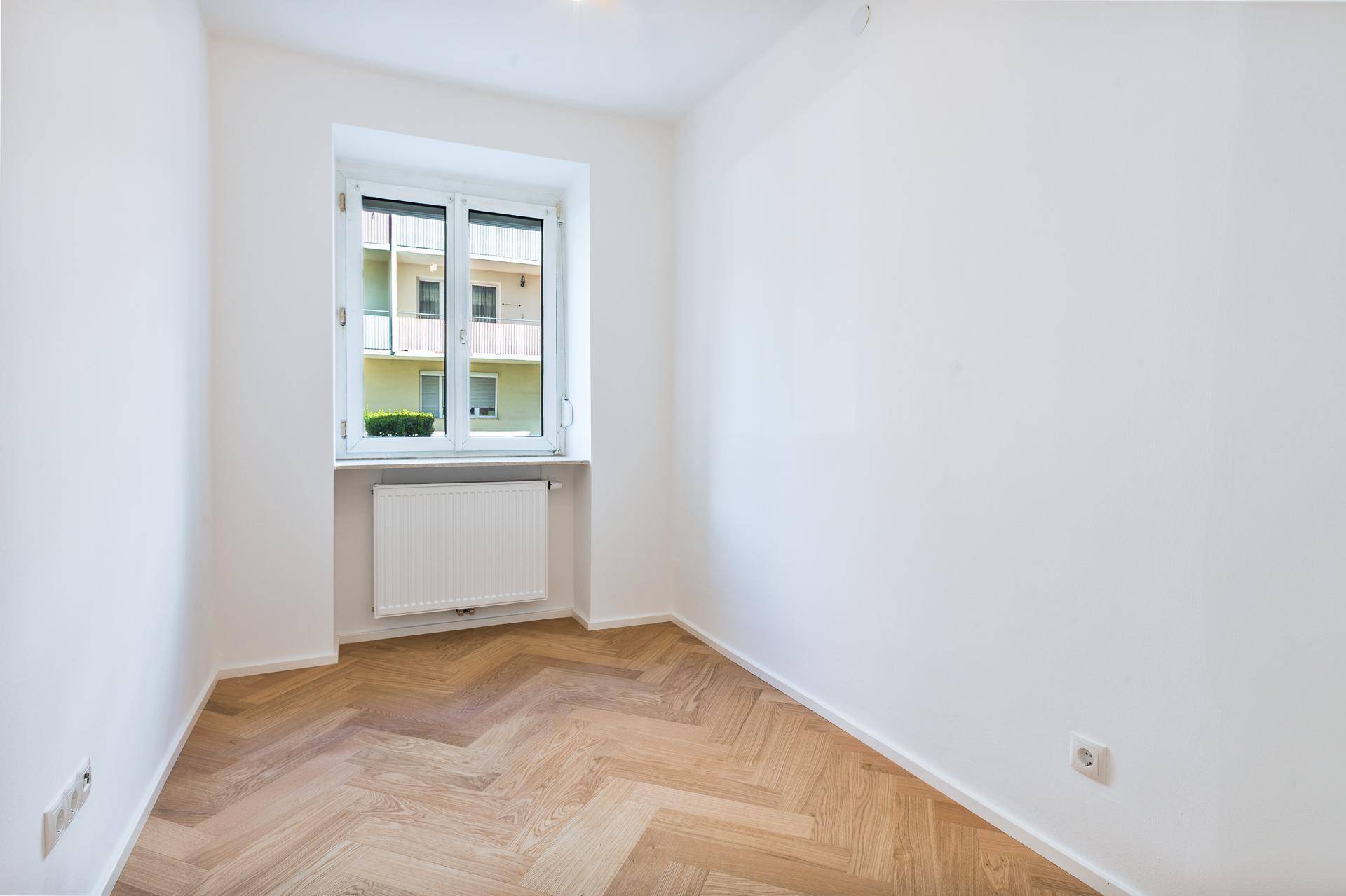 Kleineres Zimmer mit Fischgrätparkett, weißen Wänden und Blick auf den Innenhof.