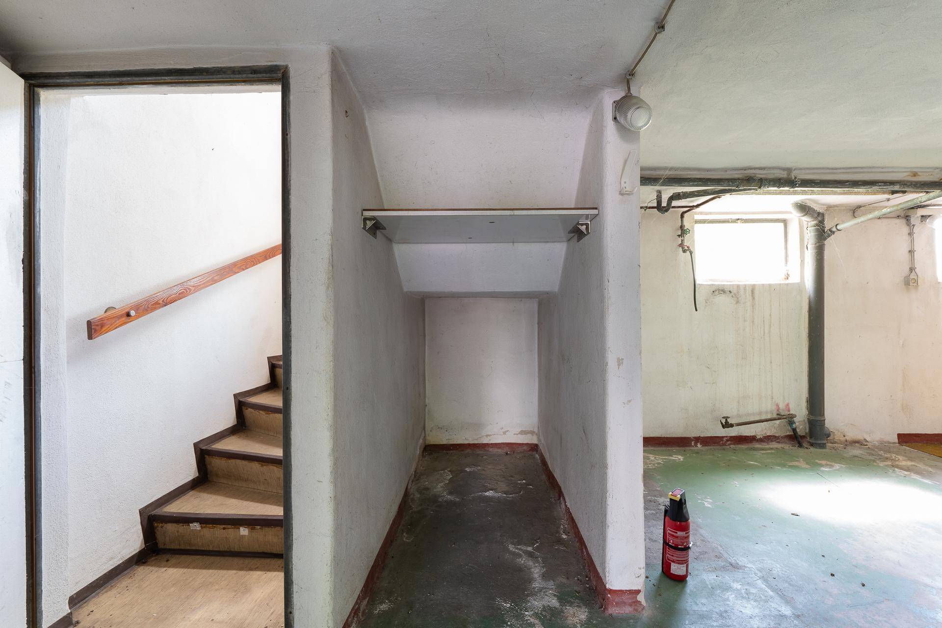 Kellerraum mit Treppenzugang und einfacher Ablagefläche.