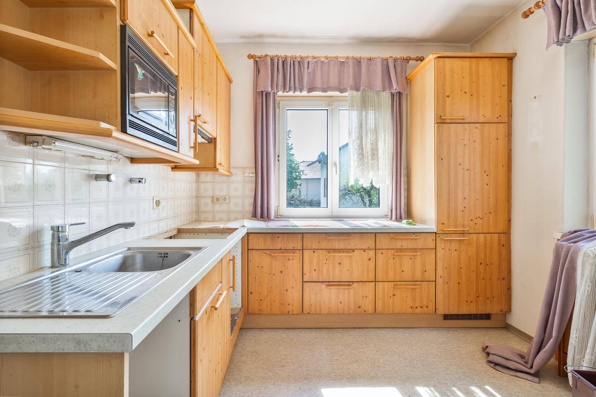 Geräumige Küche mit Holzschränken, Spüle und Fensterblick ins Grüne.