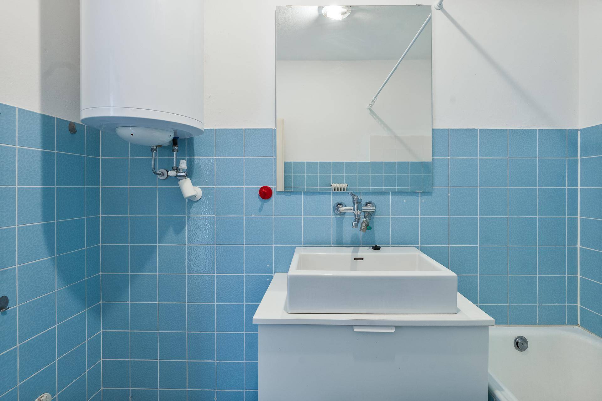 Badezimmer mit blauen Fliesen, Waschbecken und Spiegel, ausgestattet mit Warmwasserboiler.