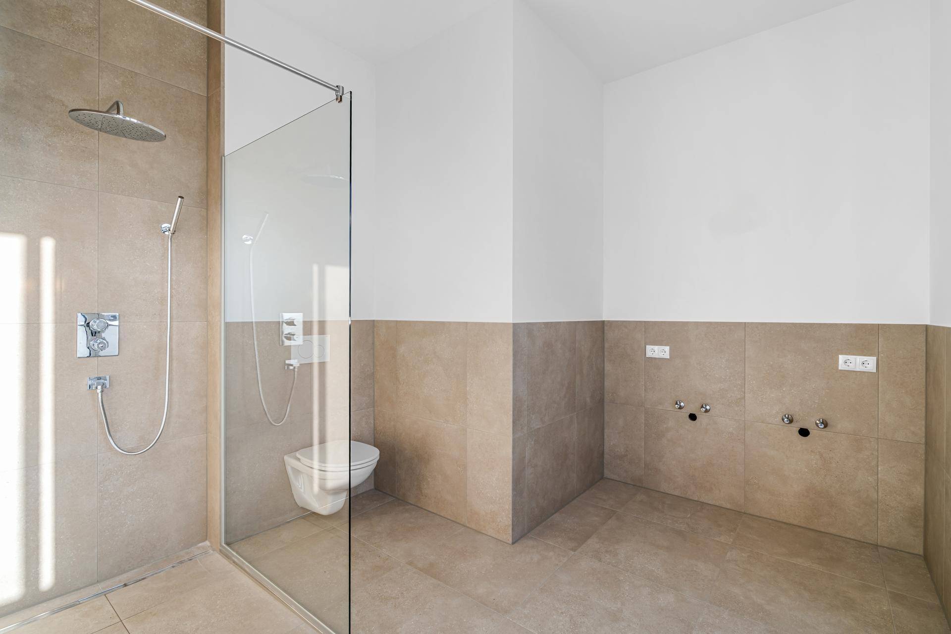 Geräumiges Badezimmer mit begehbarer Dusche, Wand-WC und Anschlüssen für einen Doppelwaschtisch.