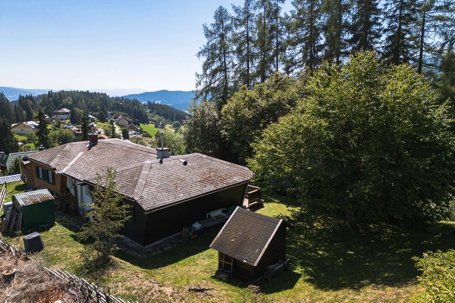 Seitenansicht des Hauses mit Holzdach und Blick auf die umliegenden grünen Hügel und Wälder.